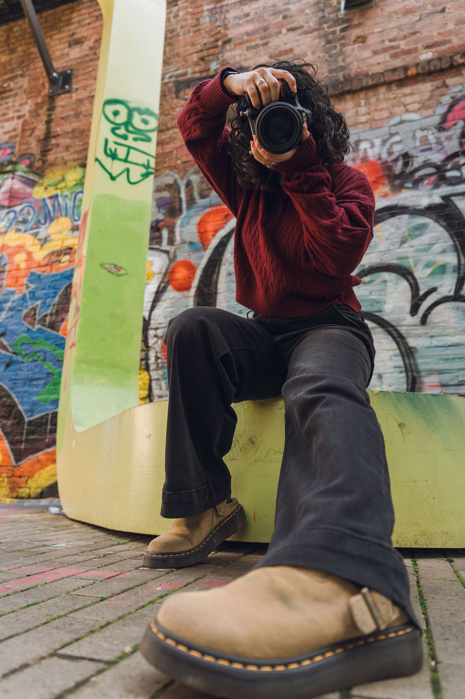 A sequence of close-up shots showing a brown leather boot with black soles against a graffiti-covered brick wall background.