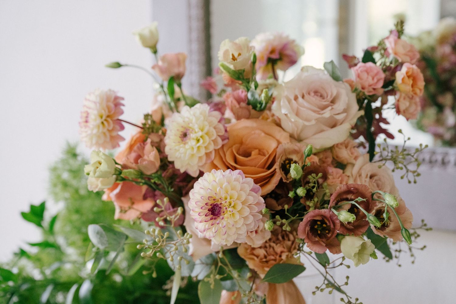 Composizione floreale romantica con rose rosa cipria, dalie e vegetazione delicata in morbidi toni pastello.