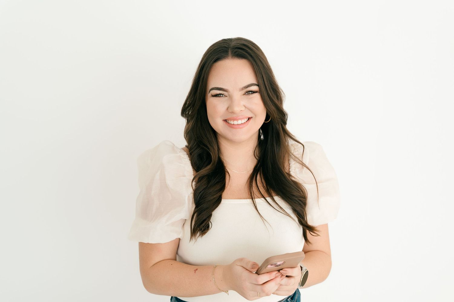 Professional portrait of woman in white top against plain backdrop.