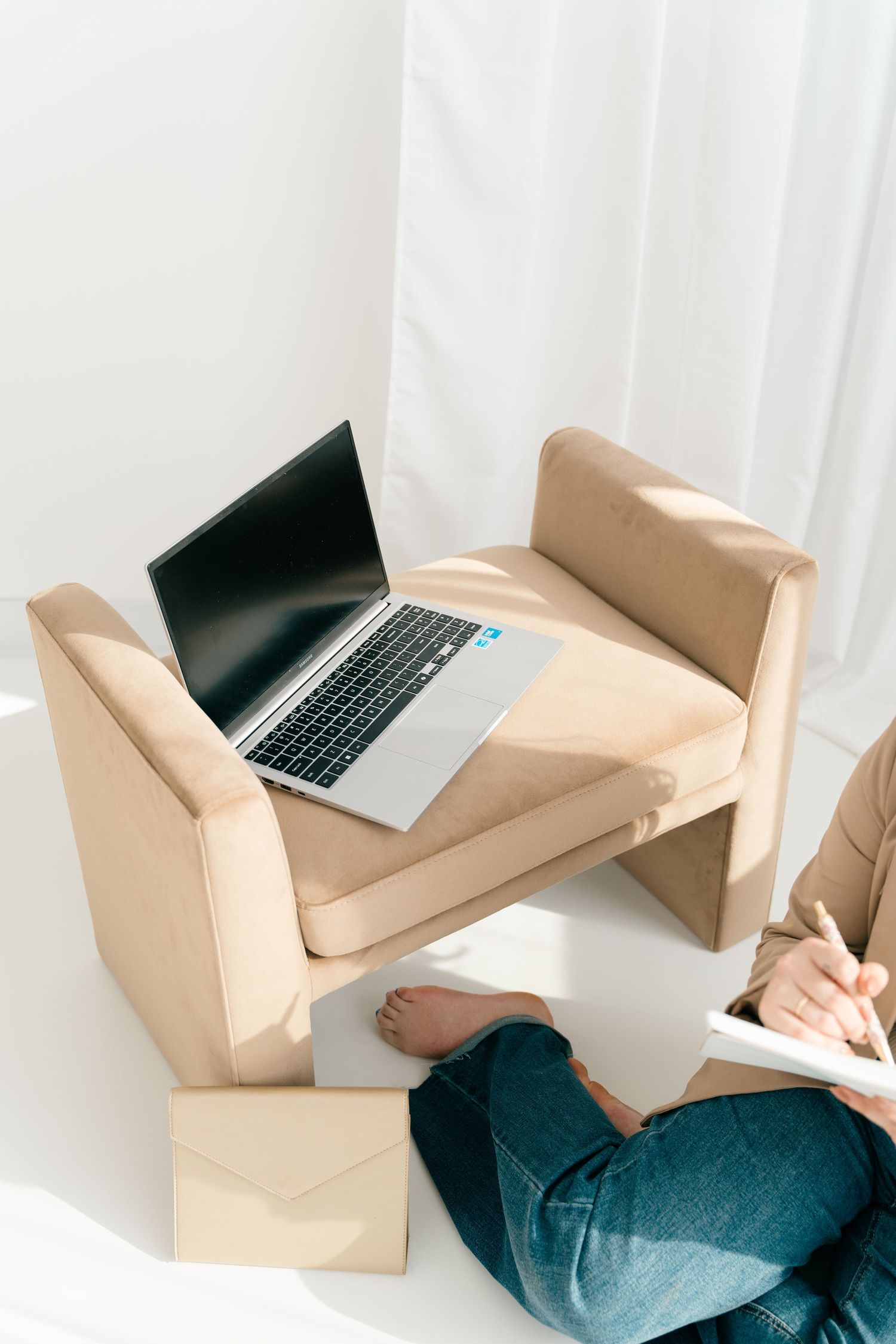 Laptop on beige cushioned chair with person writing in notebook.