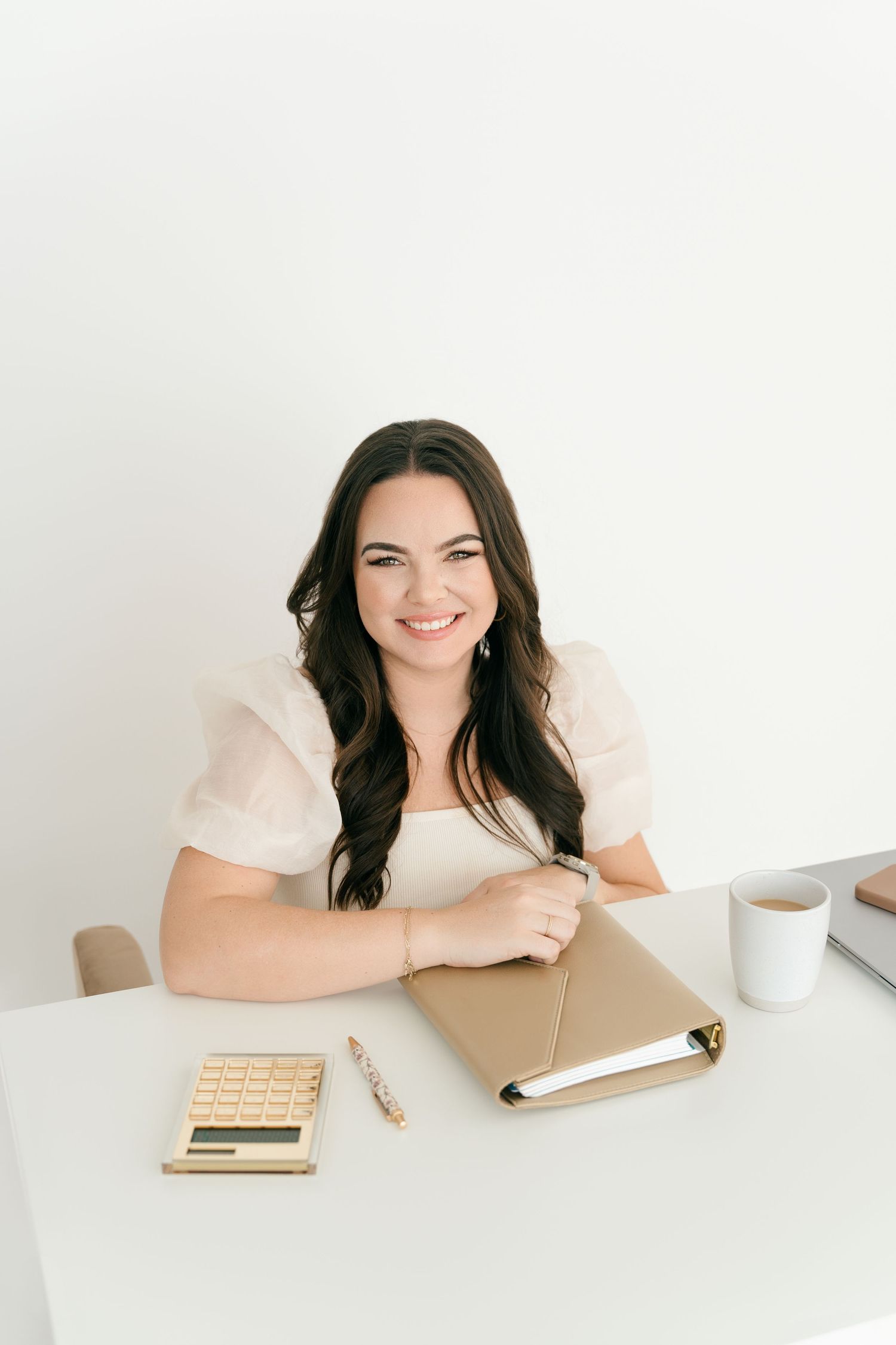Woman at desk smiling while writing in planner with coffee and calculator nearby.