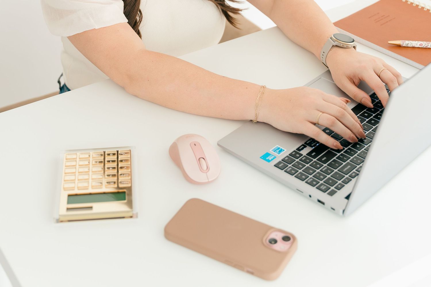 Hands typing on laptop with calculator and phone on white desk workspace.