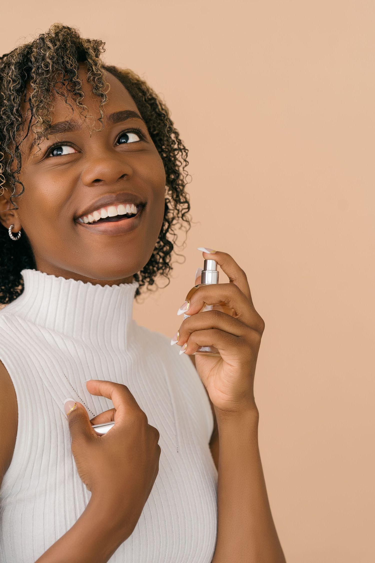 Person in white turtleneck smiling while applying fragrance.