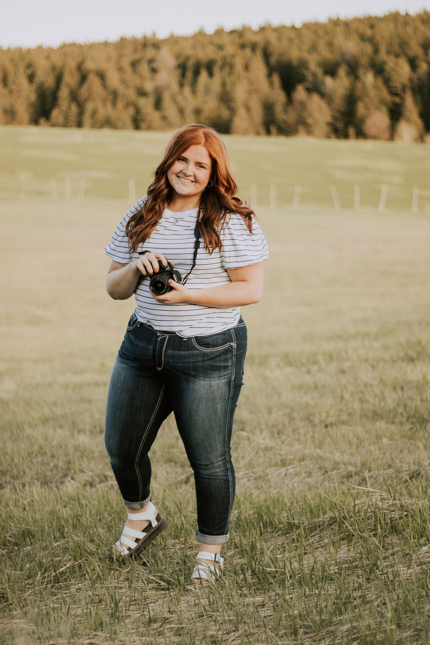 Woman in jeans posing playfully in an autumn field during golden hour.