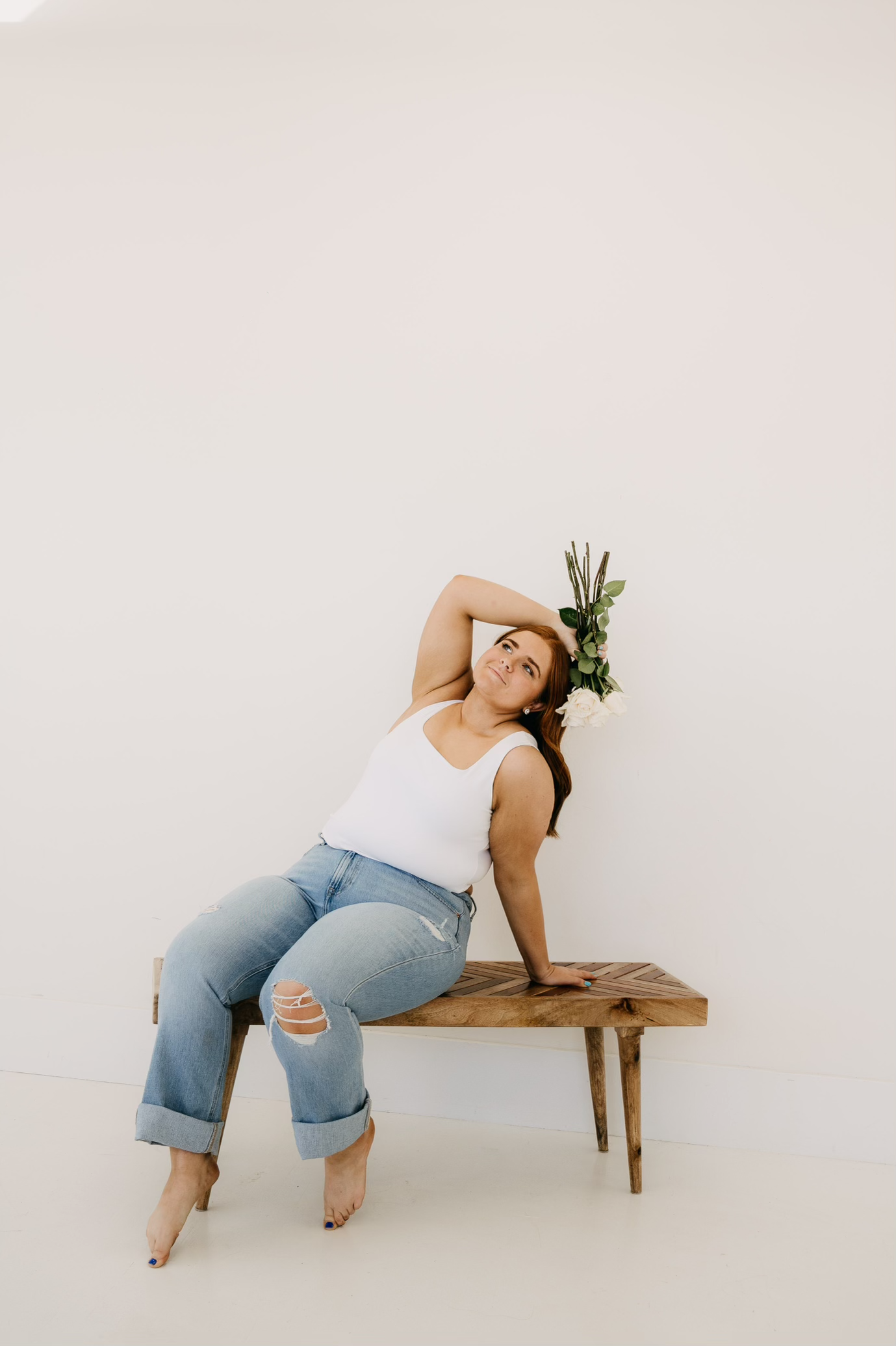 Person in casual attire reclining on a wooden bench against white background in minimalist style.