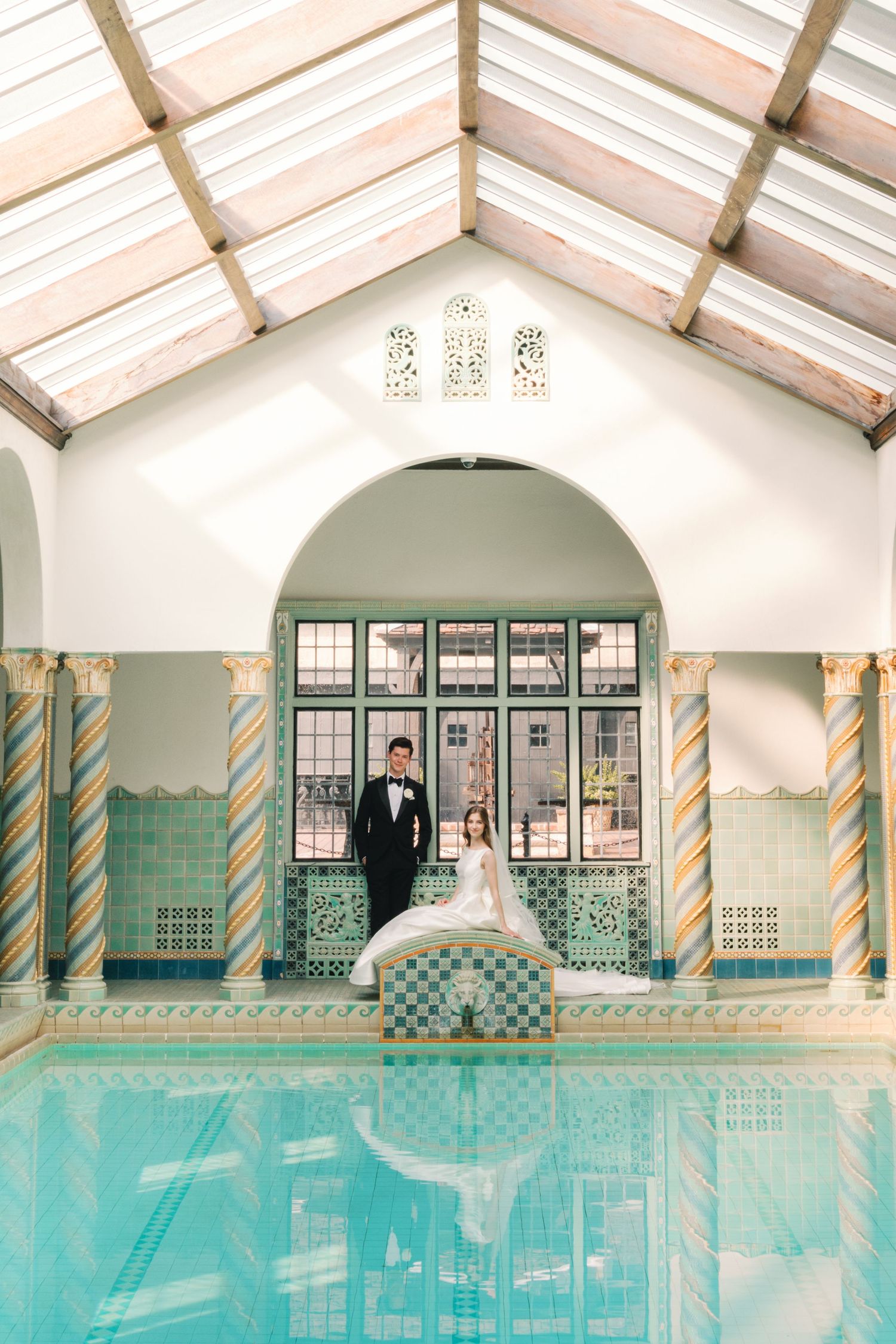 Bride and groom posing beside indoor pool in stunning tiled Mediterranean wedding venue.