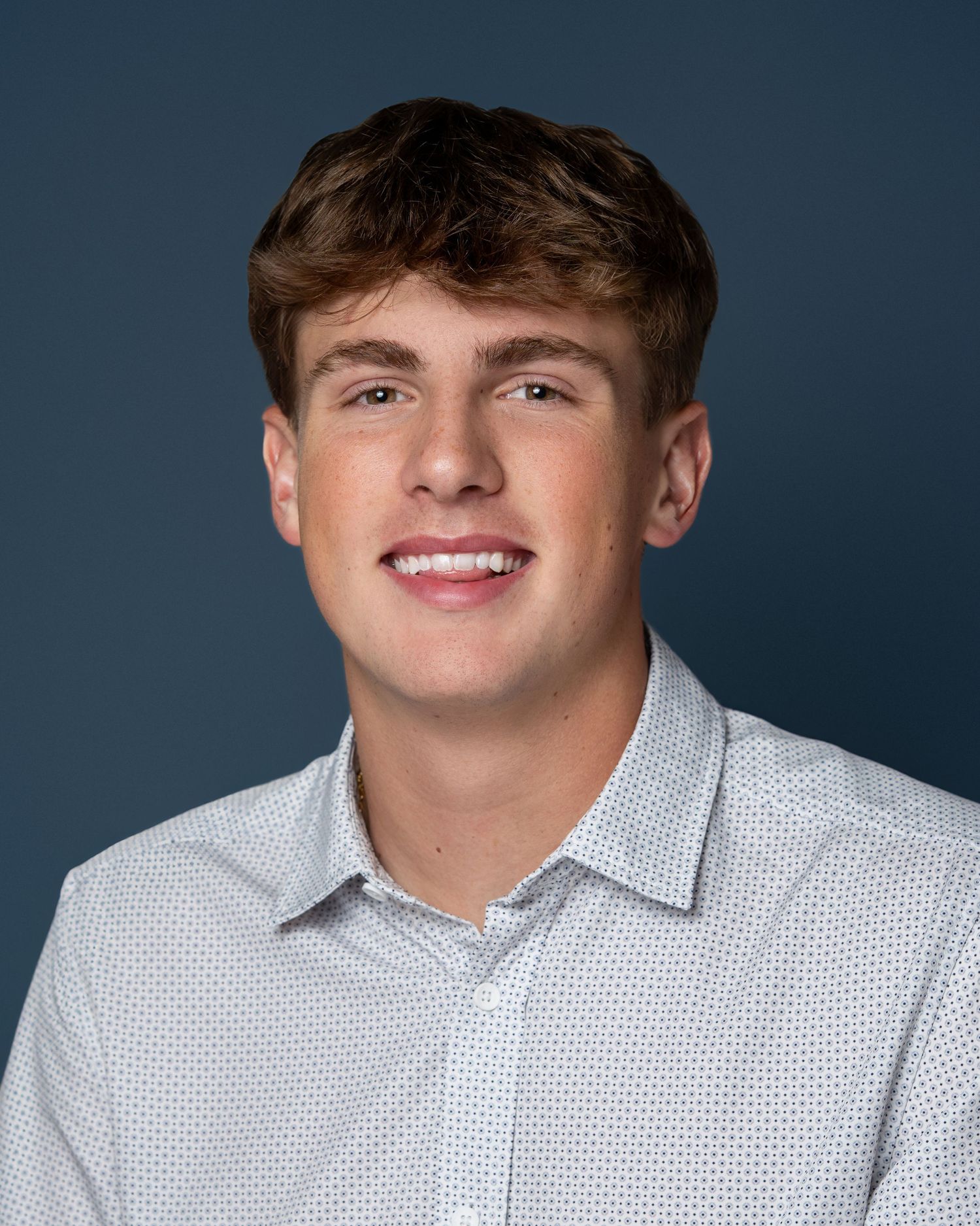 Walnut Hills School Yearbook. Cincinnati, Ohio. Senior with brown hair smiling in a white button-up shirt against a dark blue background.