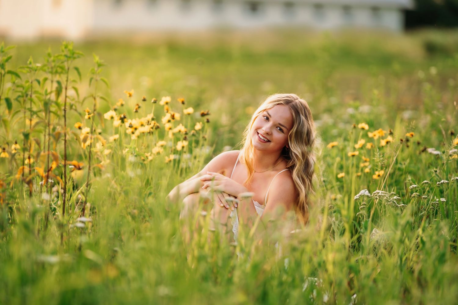 Senior photography in Cincinnati. A woman in a white dress lies in a sunny meadow filled with yellow wildflowers and tall grass.