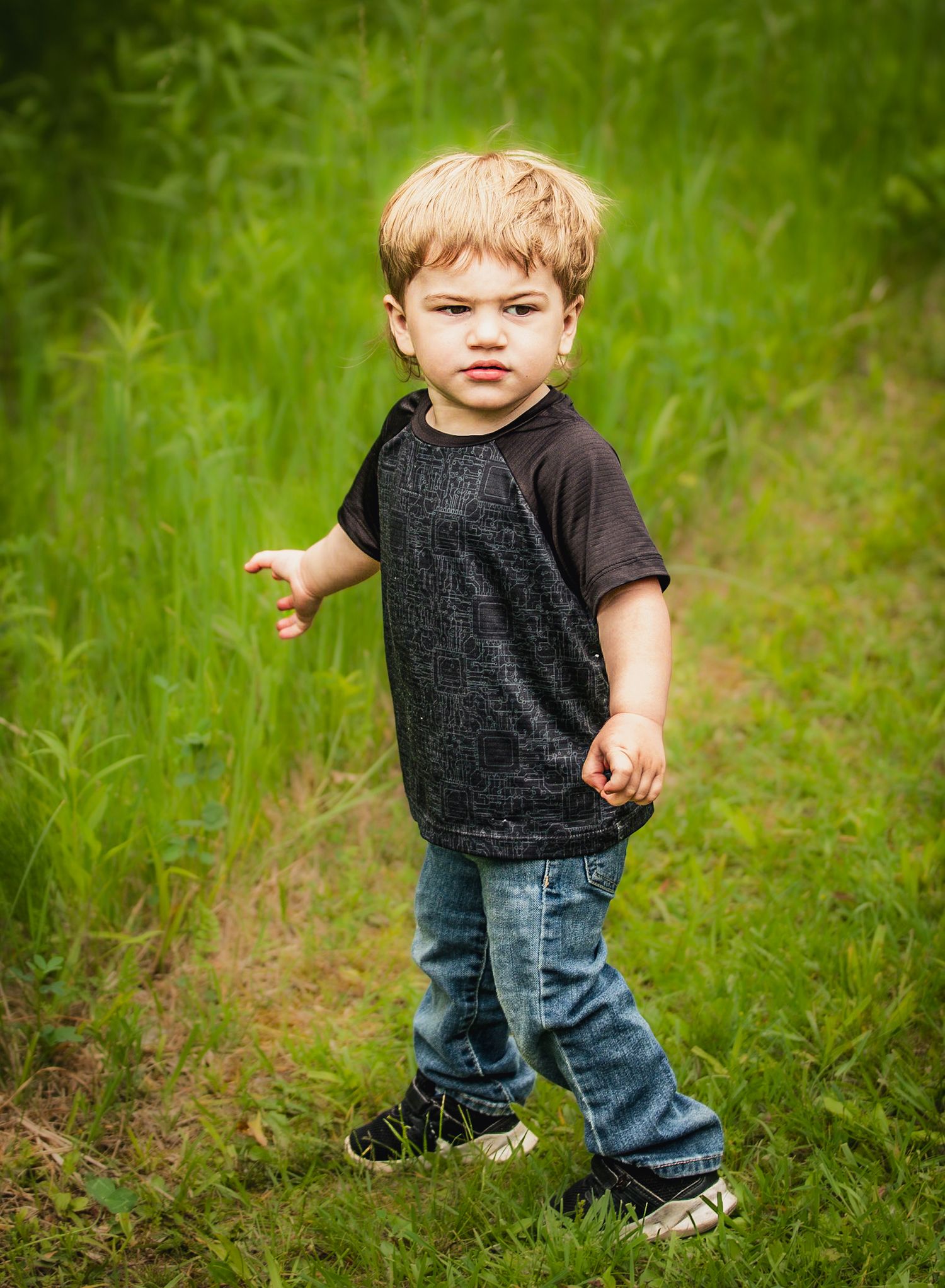 A child wearing jeans and a dark shirt explores a grassy field.