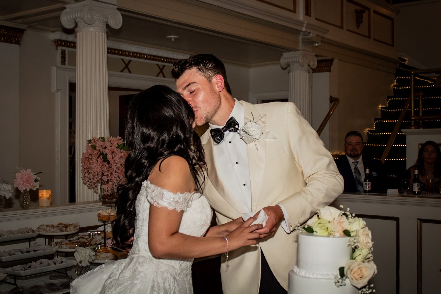 A bride and groom share a romantic dance during their wedding reception near an elegant white wedding cake.