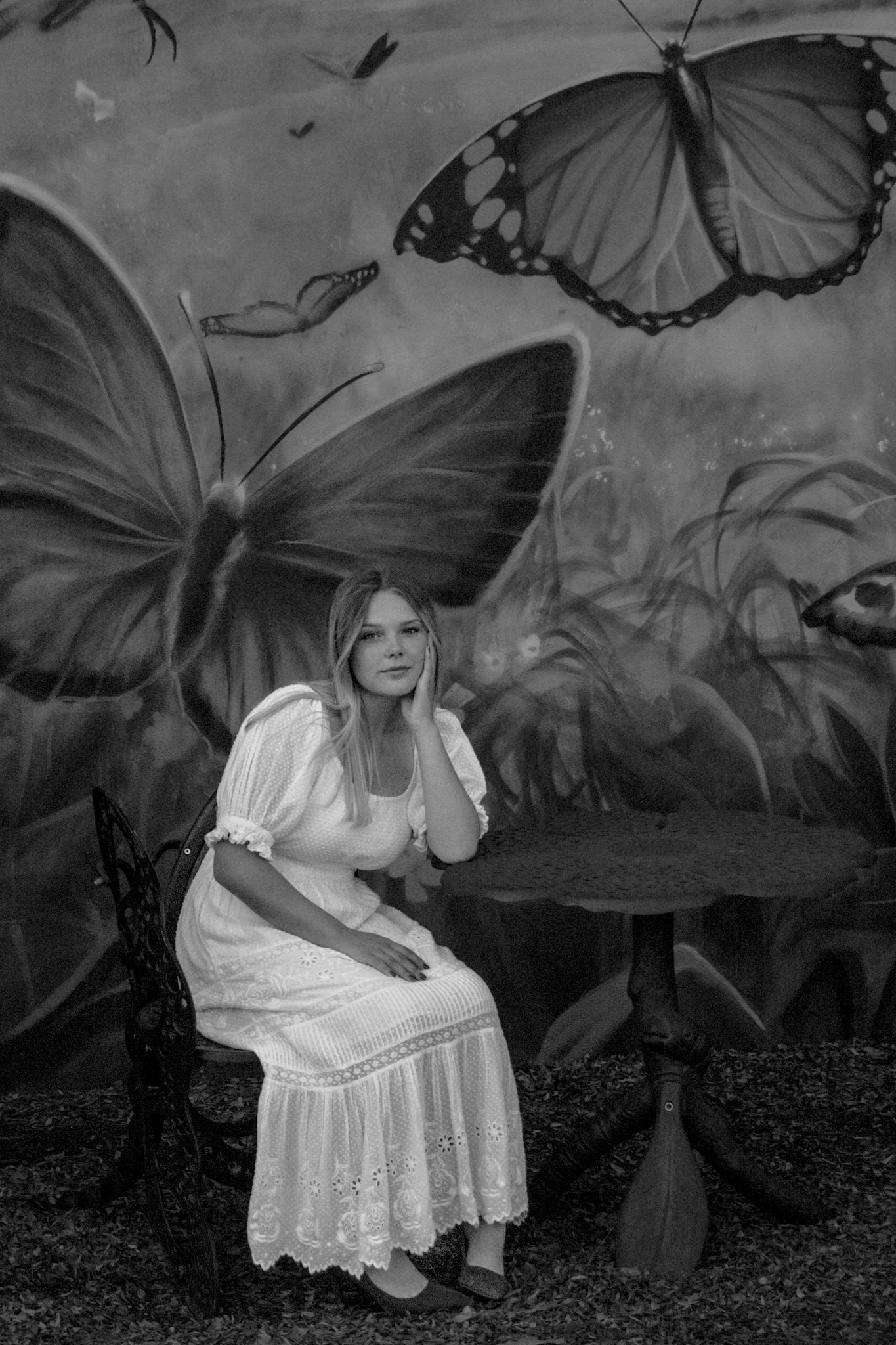 A person in a white dress sitting against a wall with painted butterfly murals.