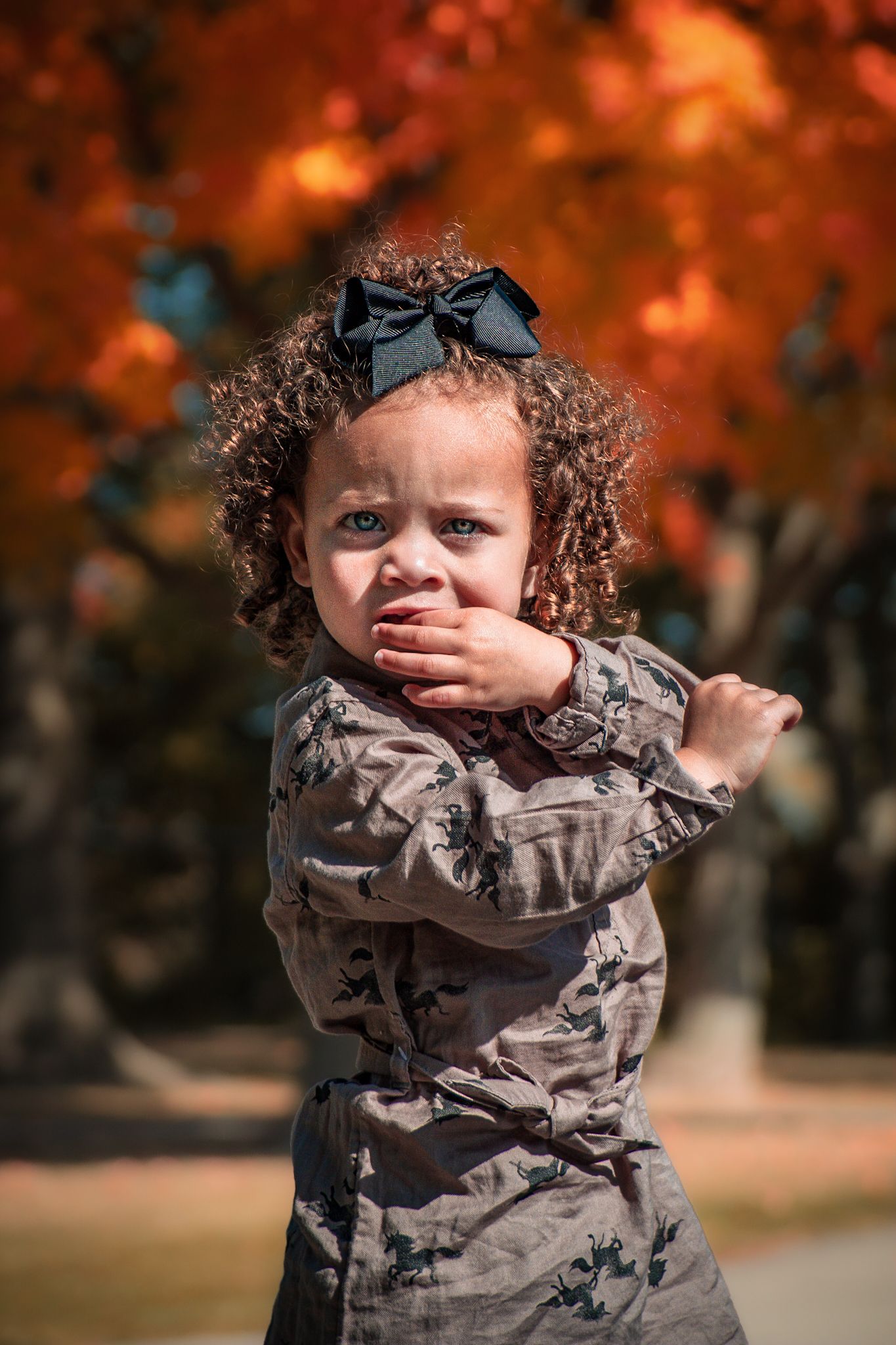 A small child wearing a camouflage jacket poses against an autumn background.