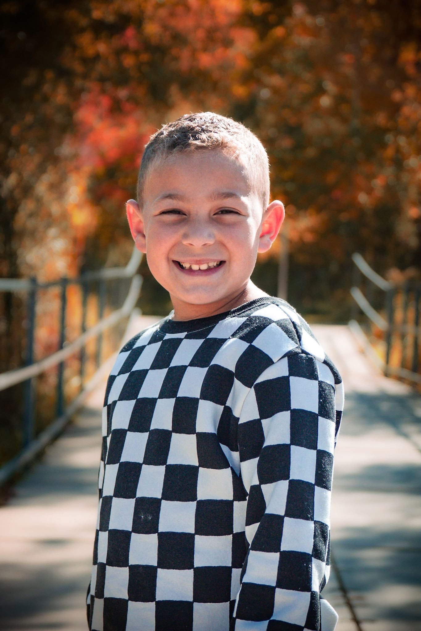 A person wearing a checkered black and white jacket smiles outdoors in autumn.