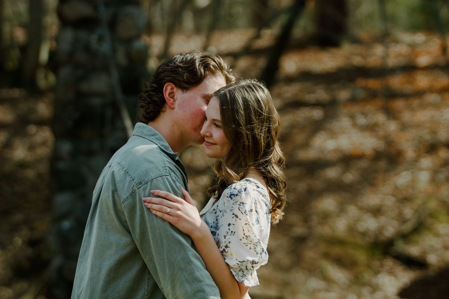 Couple shares an intimate embrace in a wooded setting with warm natural lighting.