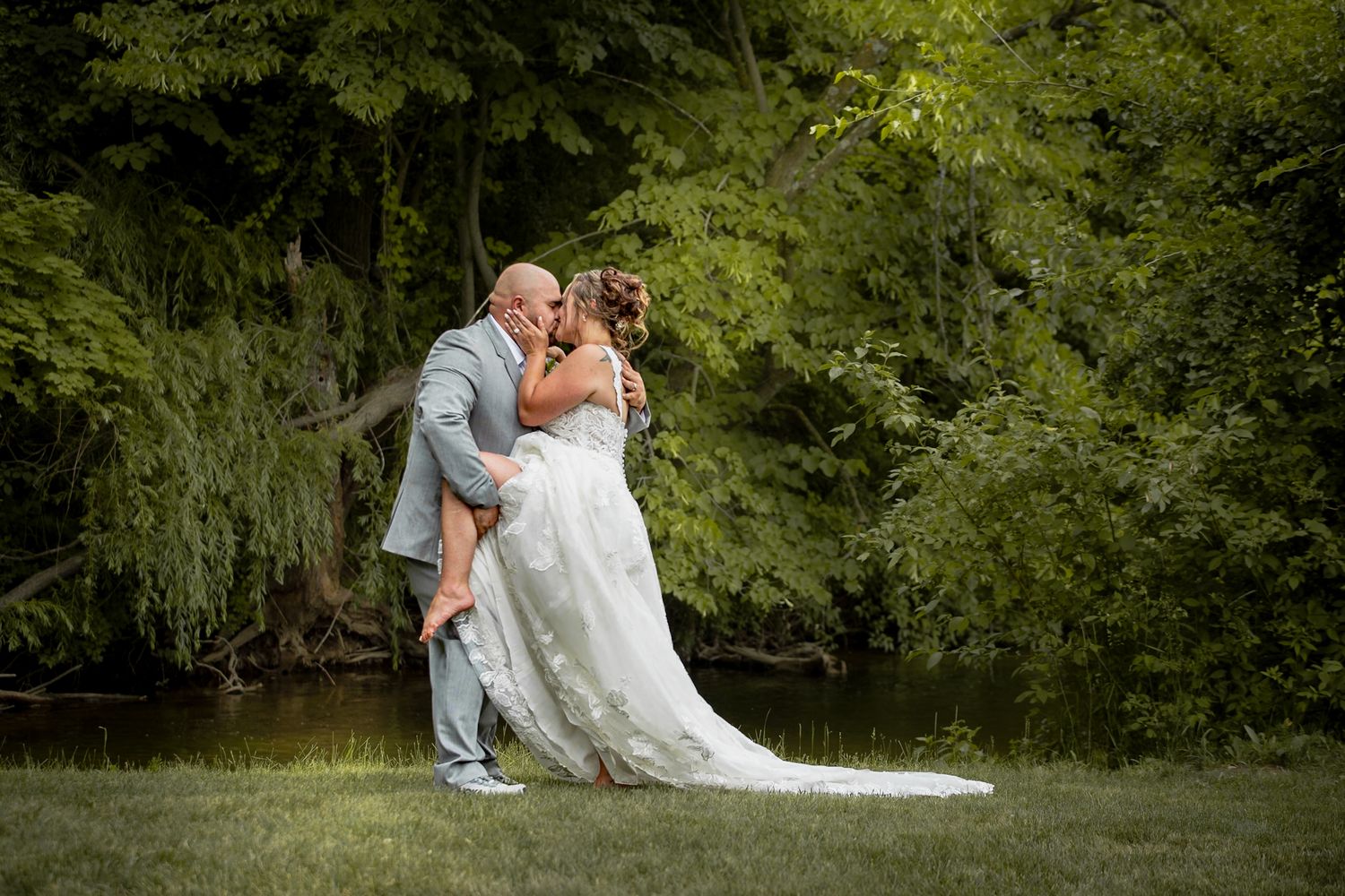 A playful wedding portrait by a pond with flowing white dress at Riverwalk Place venue in Gladwin Michigan.