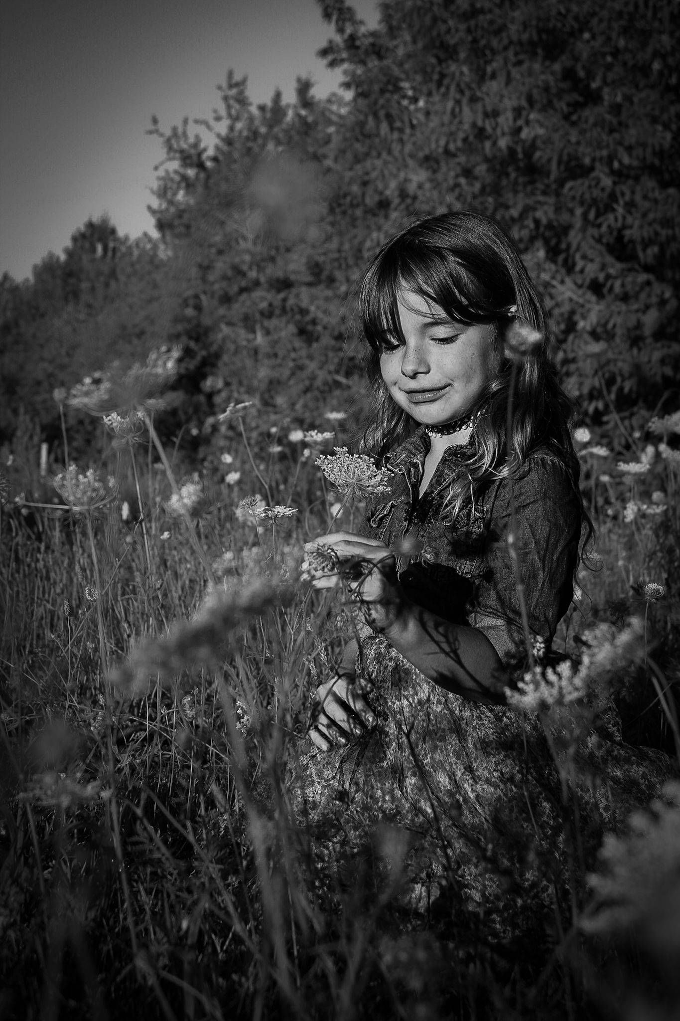 Black and white portrait of someone gathering wildflowers in a meadow at sunset.