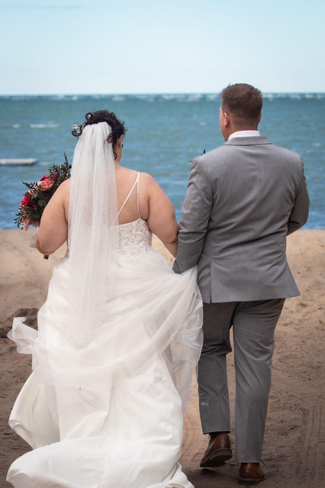 Newlyweds walking together on a beach with flowing wedding dress and ocean view.