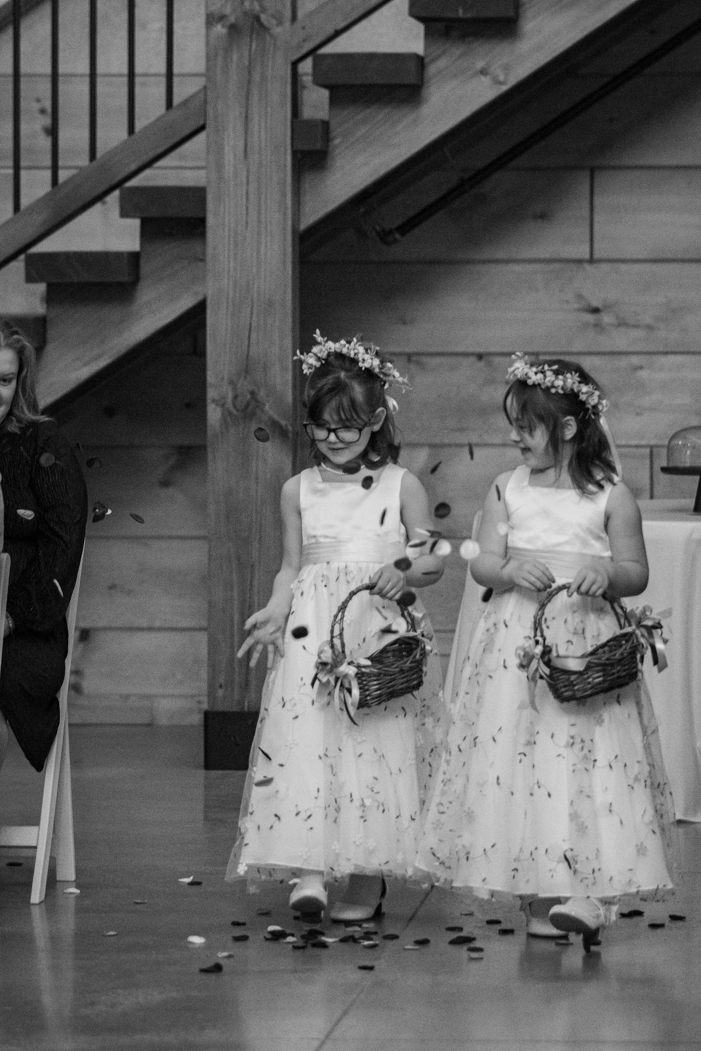 Two flower girls in white dresses and floral crowns hold baskets during a wedding ceremony.