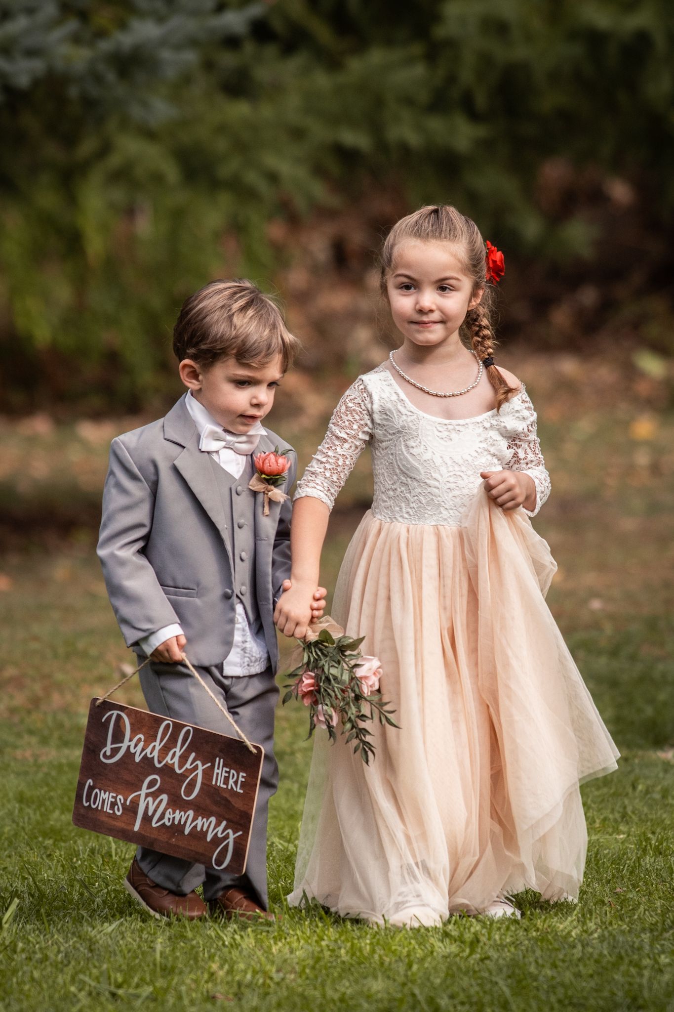 Two young children in formal attire pose with a wooden wedding sign.