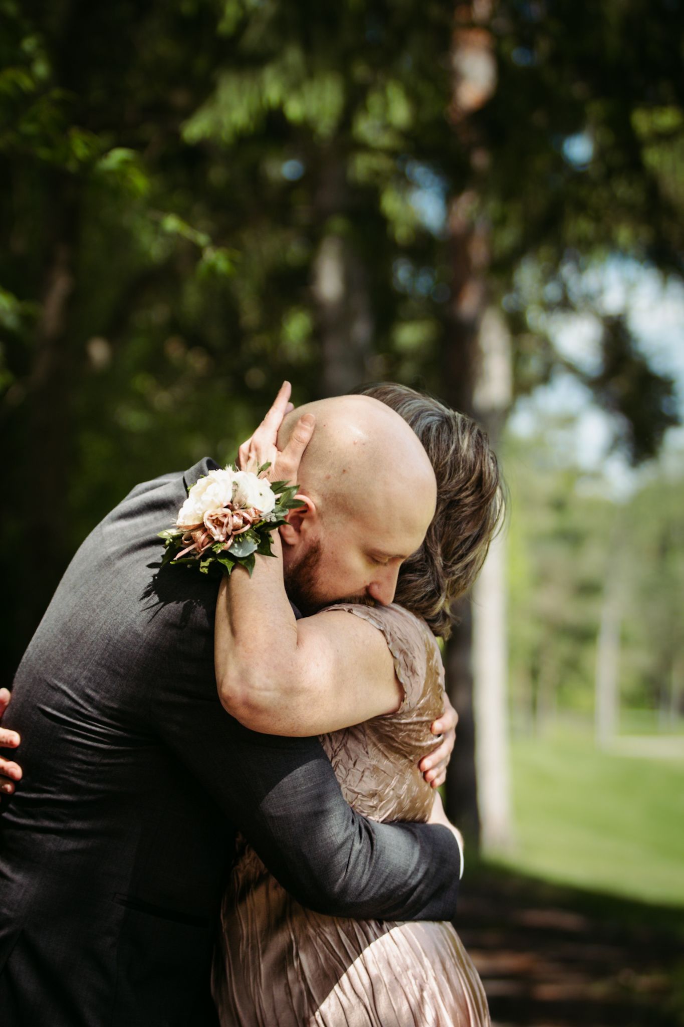 Emotional embrace captured during wedding ceremony with floral boutonniere detail.