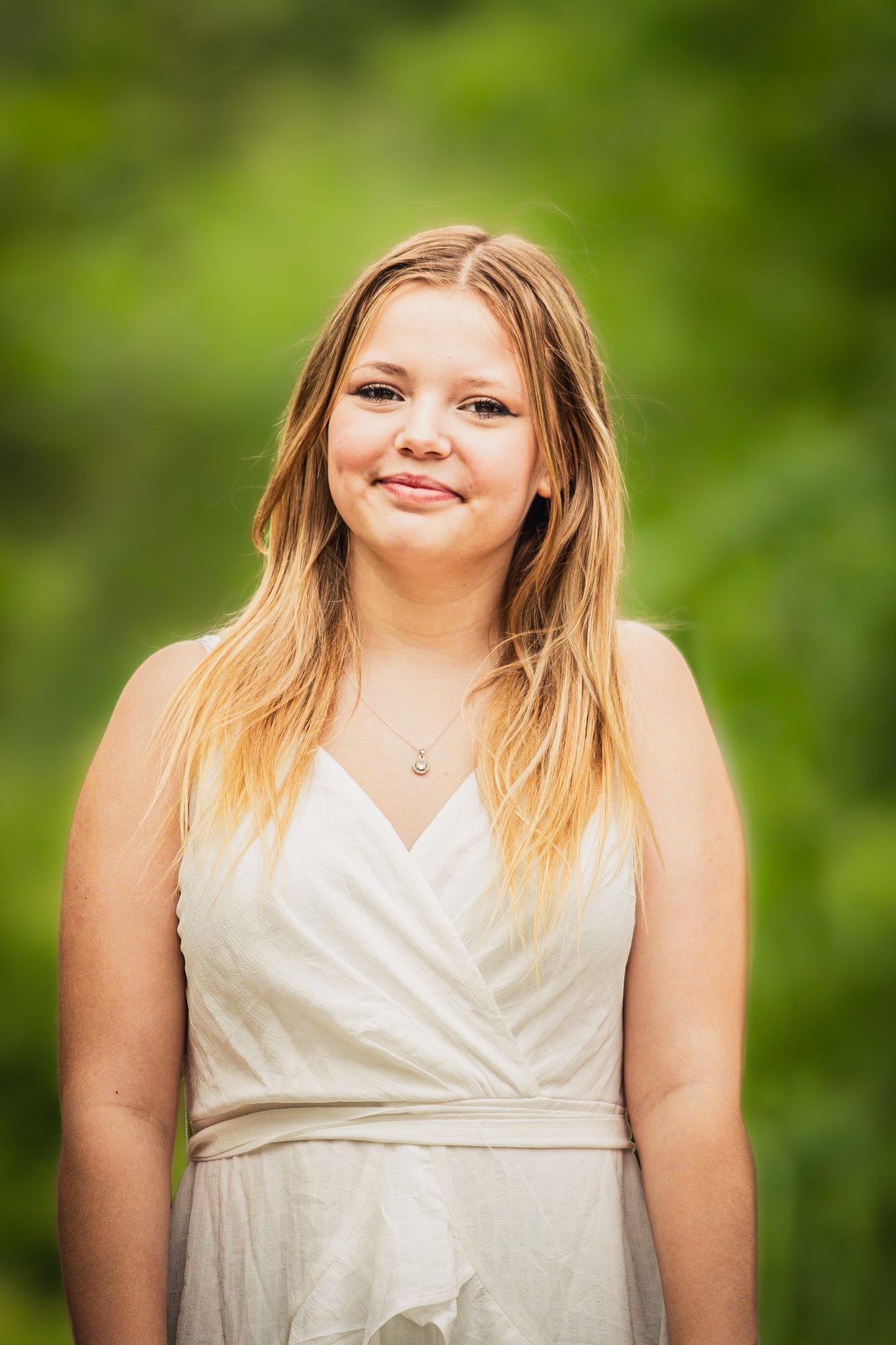 Portrait of person in cream dress smiling outdoors with natural green background.
