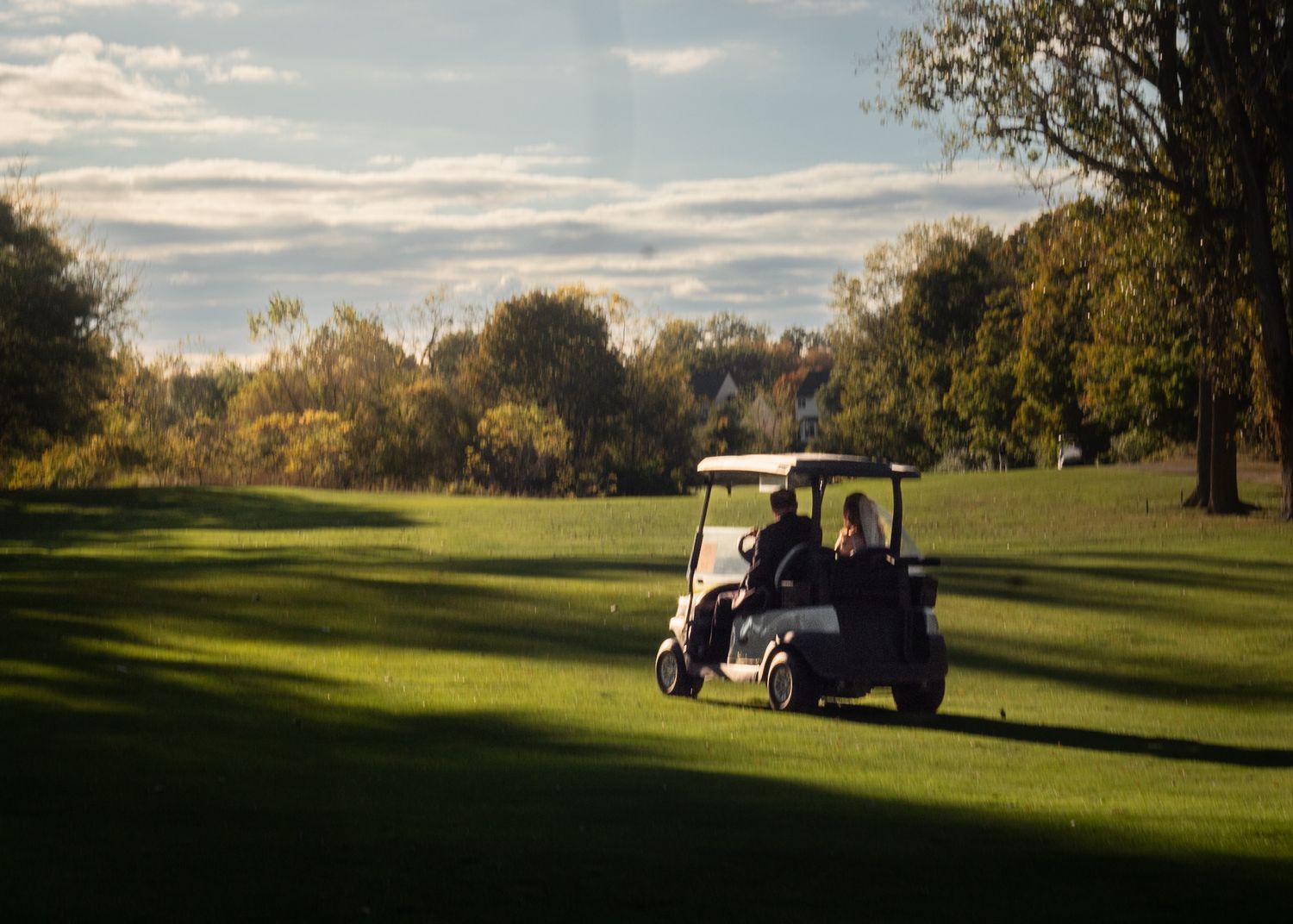 Golf cart driving across a sunlit golf course with green fairways and trees during golden hour.