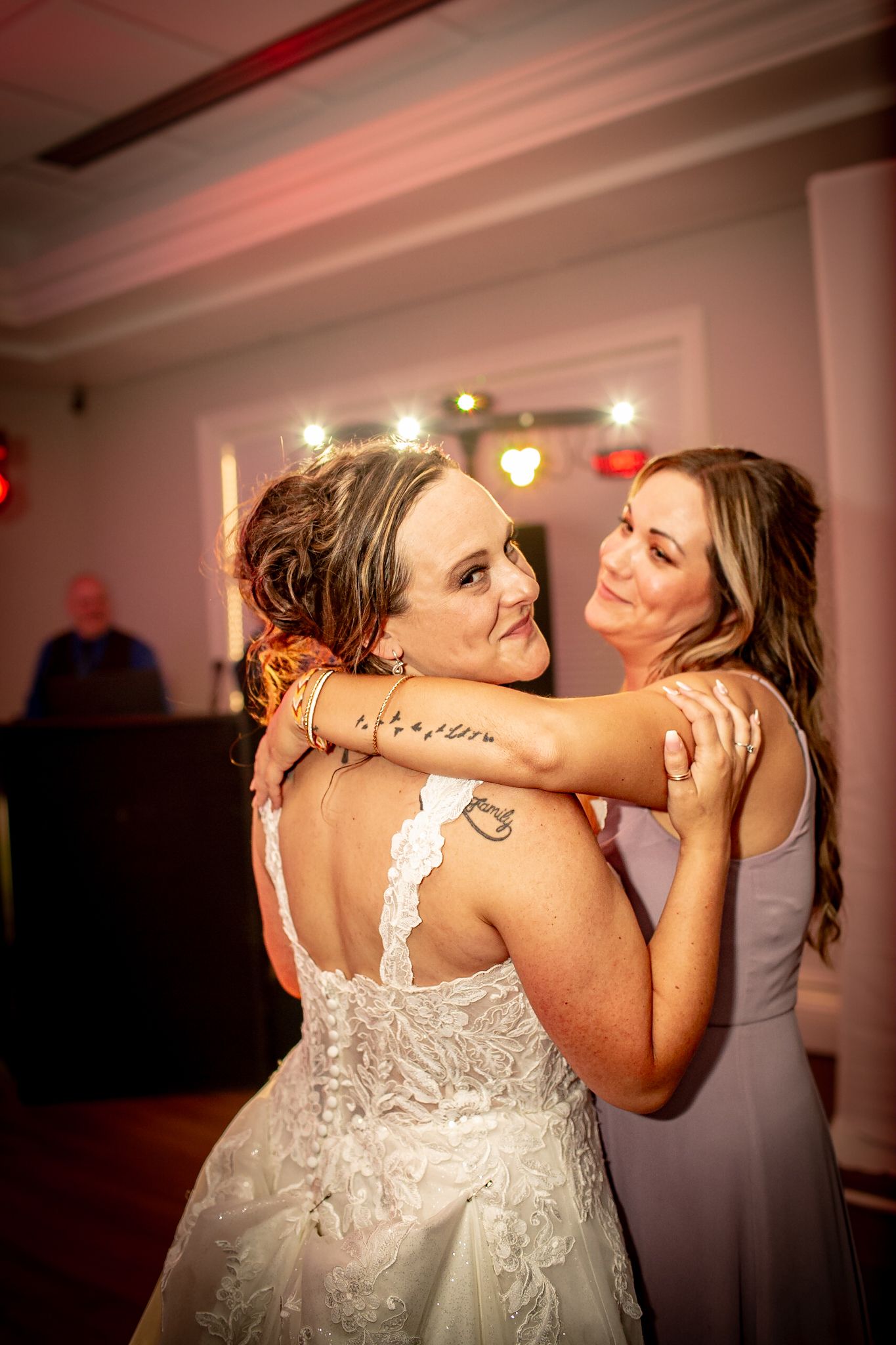 Two people embrace and dance closely together during what appears to be a wedding reception in a dimly lit room.