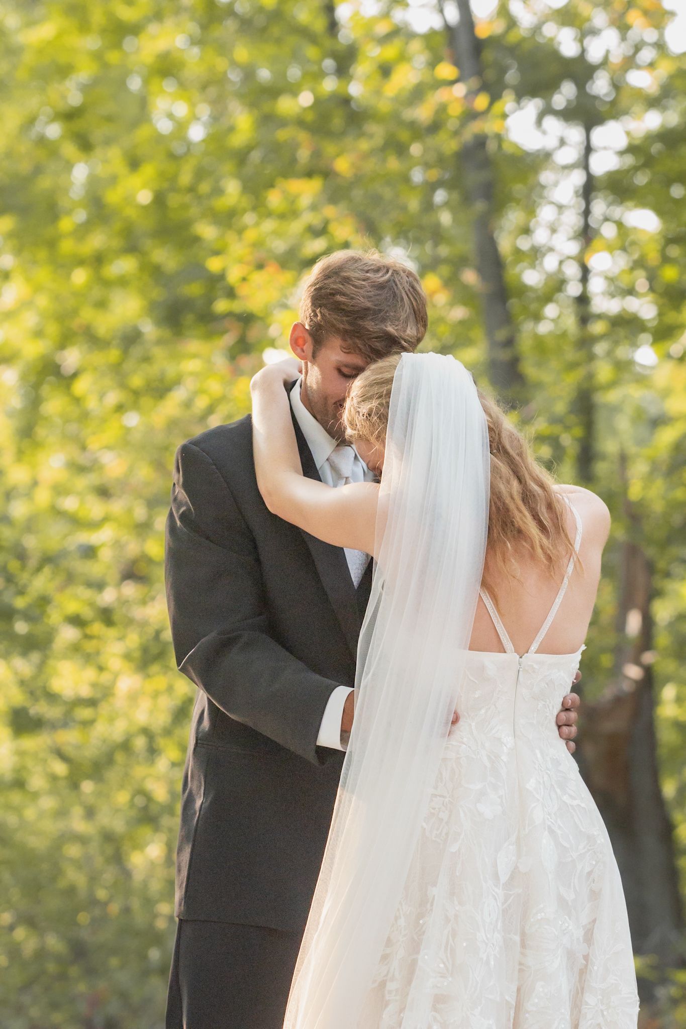 Sun-drenched wedding portrait captures intimate embrace between newlyweds in autumn forest setting.