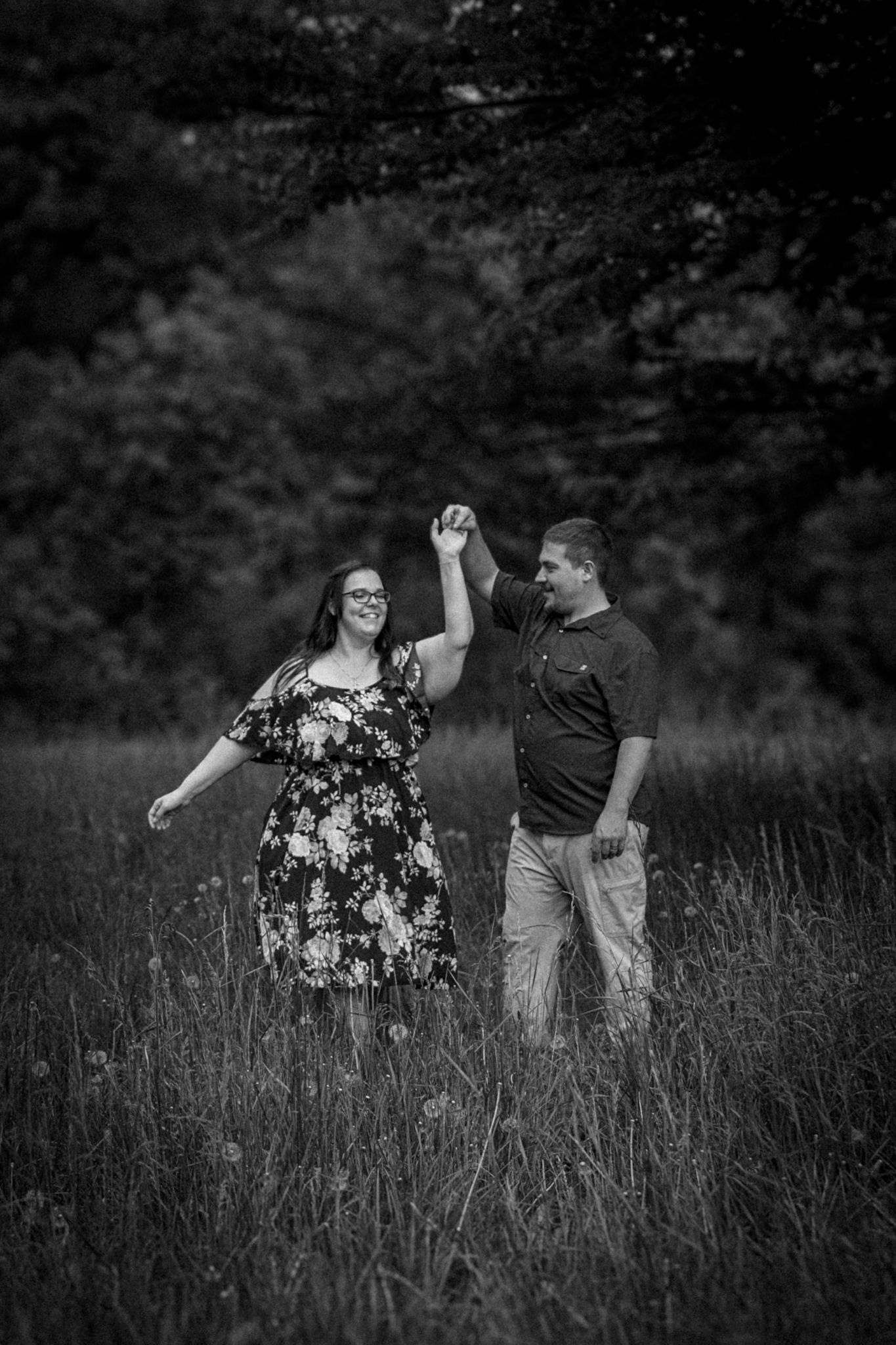 Couple dancing joyfully in field during black and white engagement photoshoot.