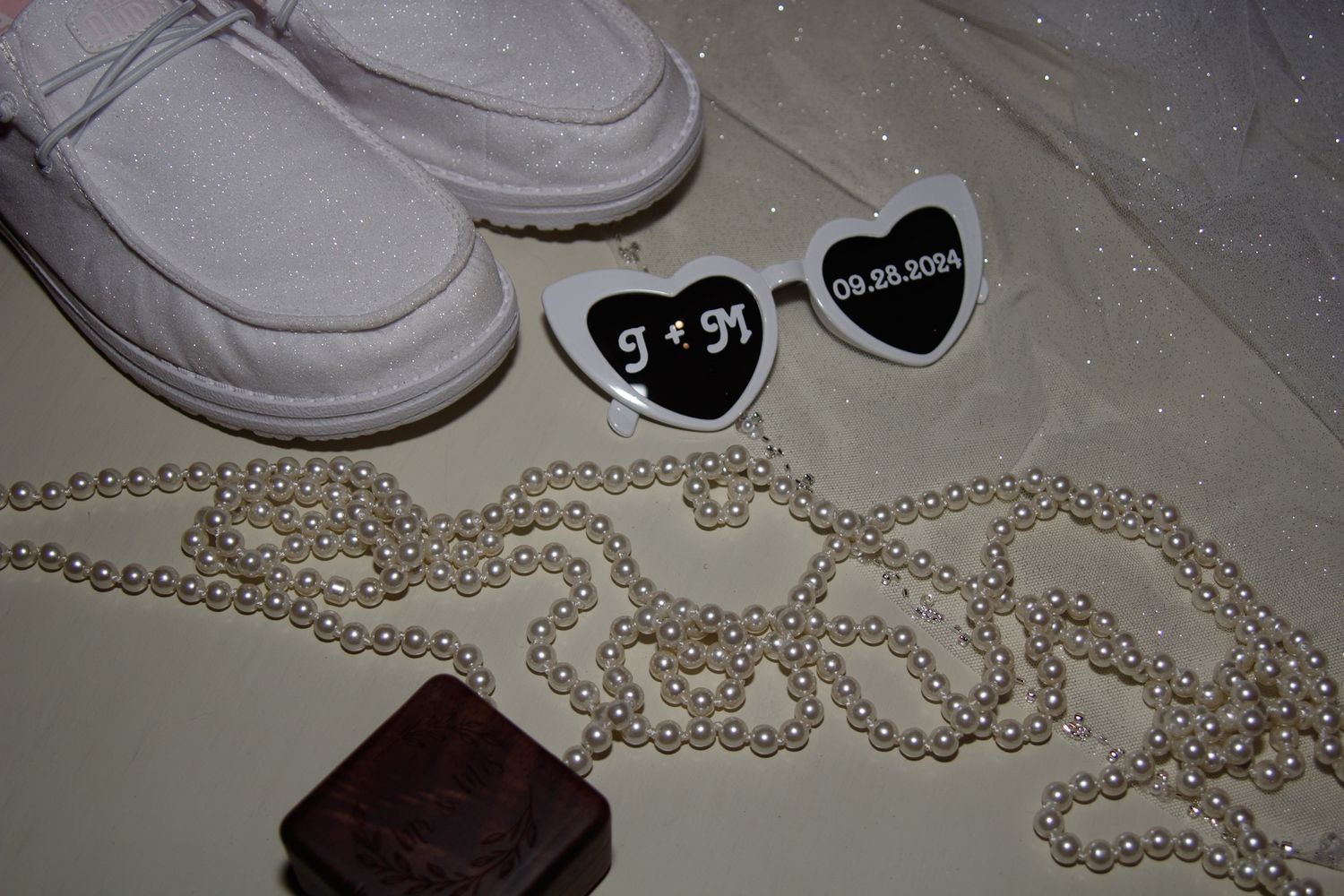 Wedding accessories including heart-shaped pins, pearl necklace, and shoes on a light surface.