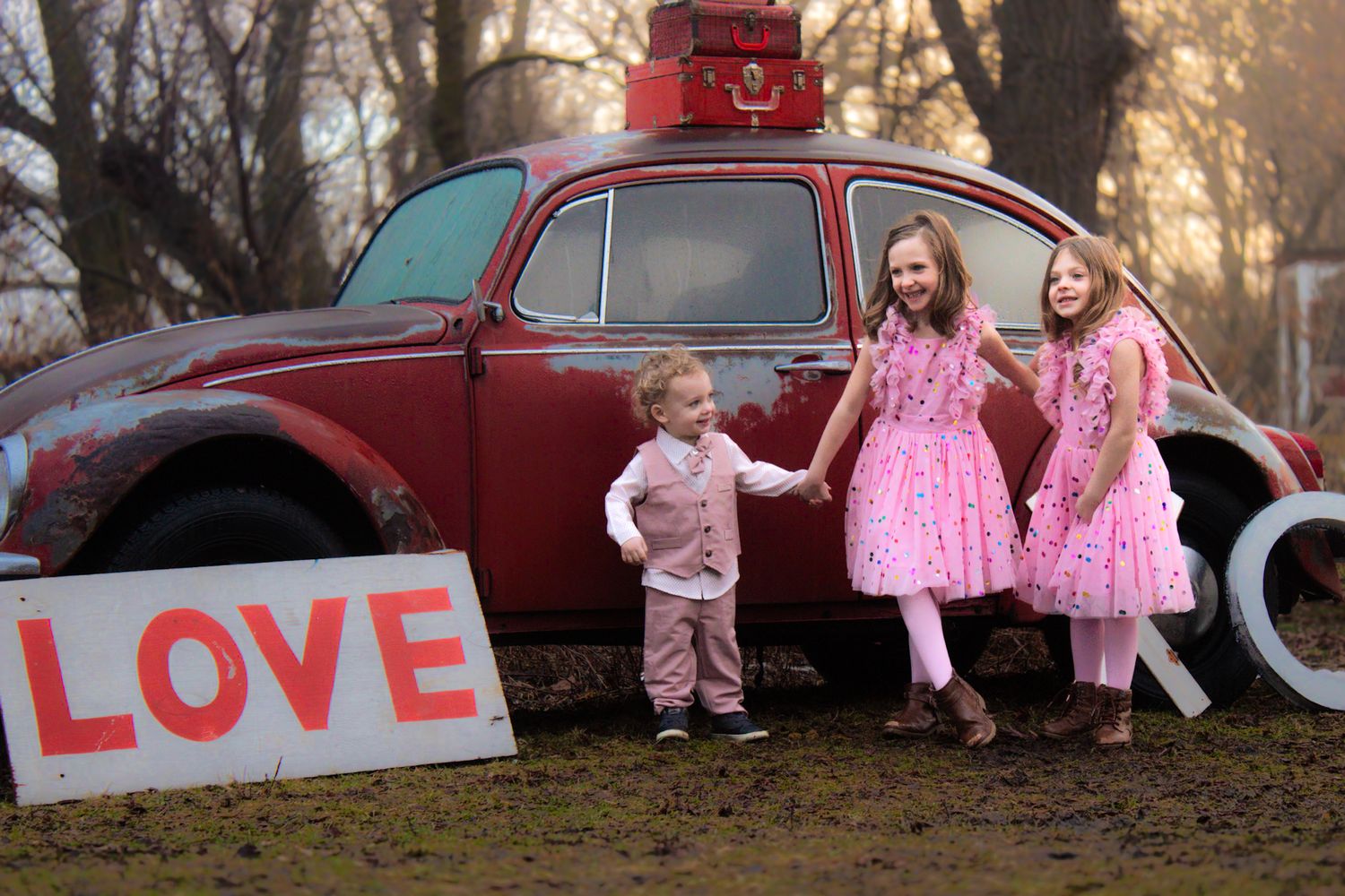 Children posing by a vintage red car during sunset.