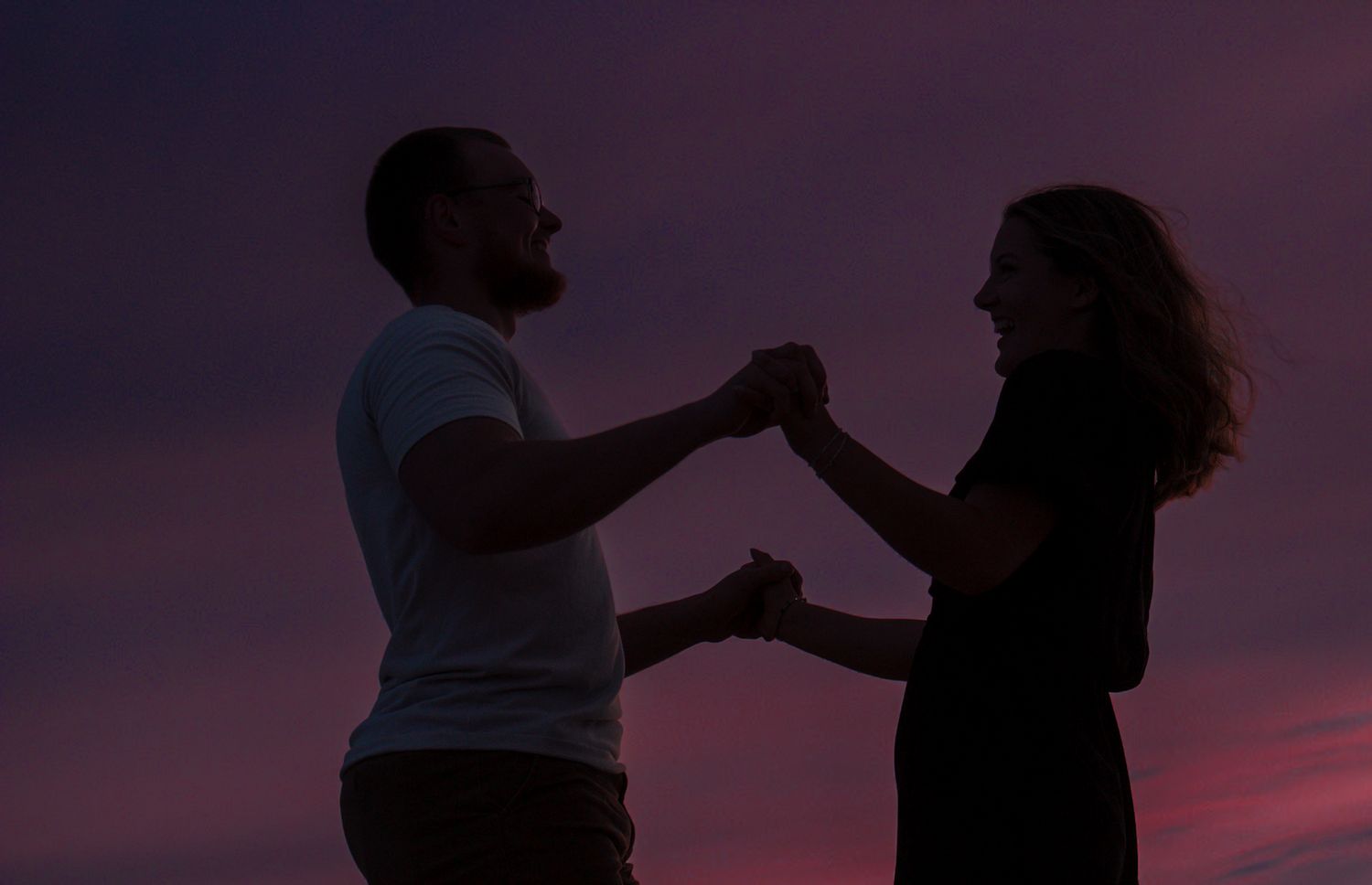 Silhouettes dancing together against purple sunset sky.