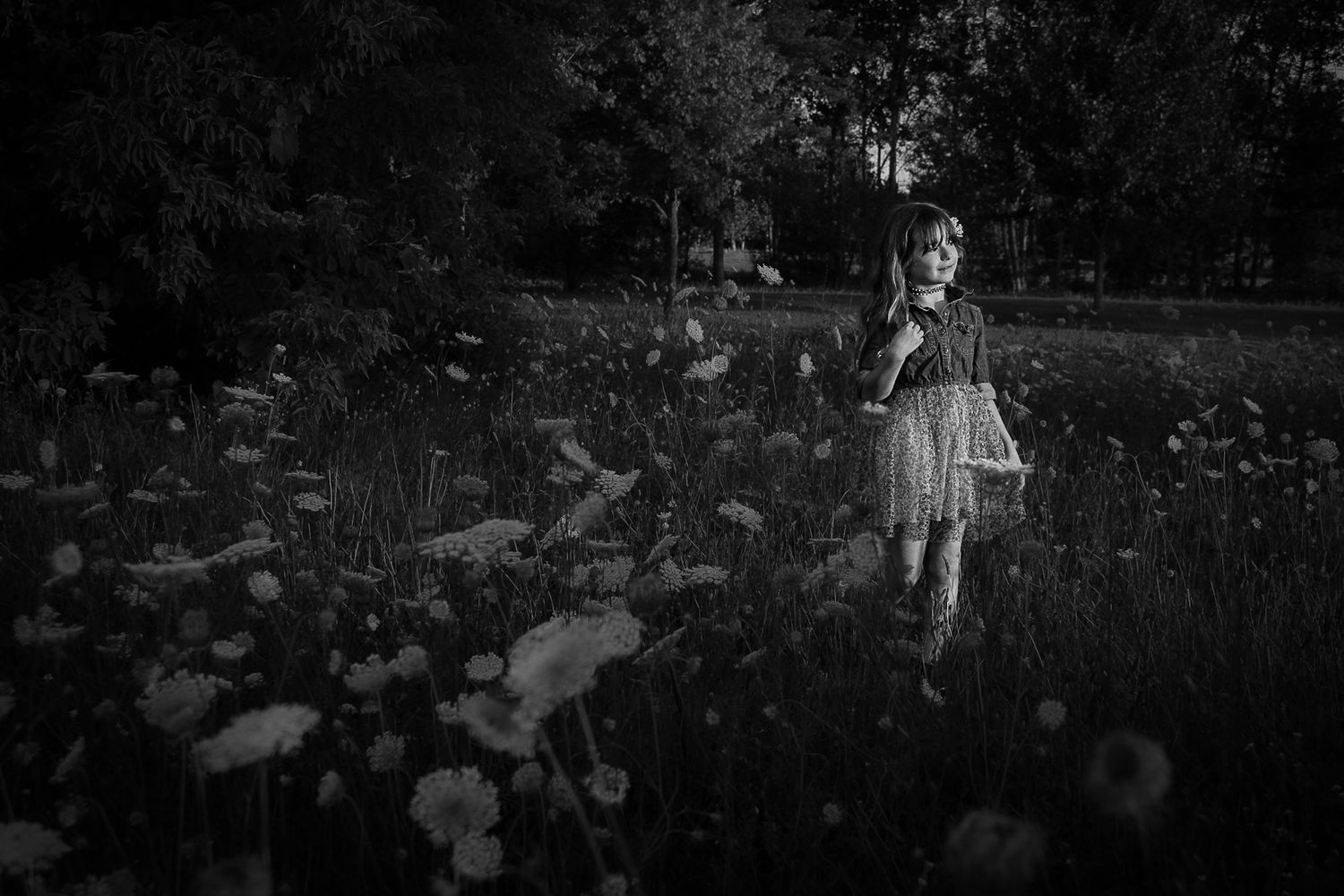 Artistic black and white portrait of child standing in field of wildflowers.