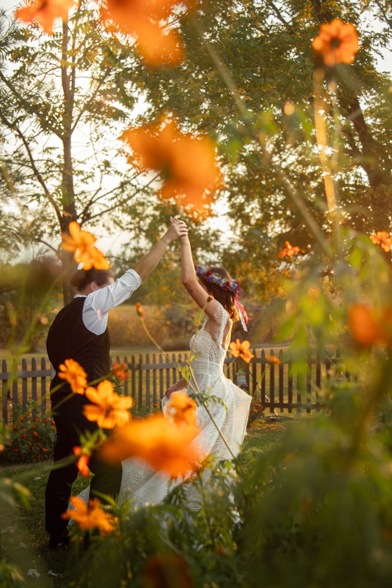 A joyful couple dancing in a garden surrounded by orange flowers at sunset.
