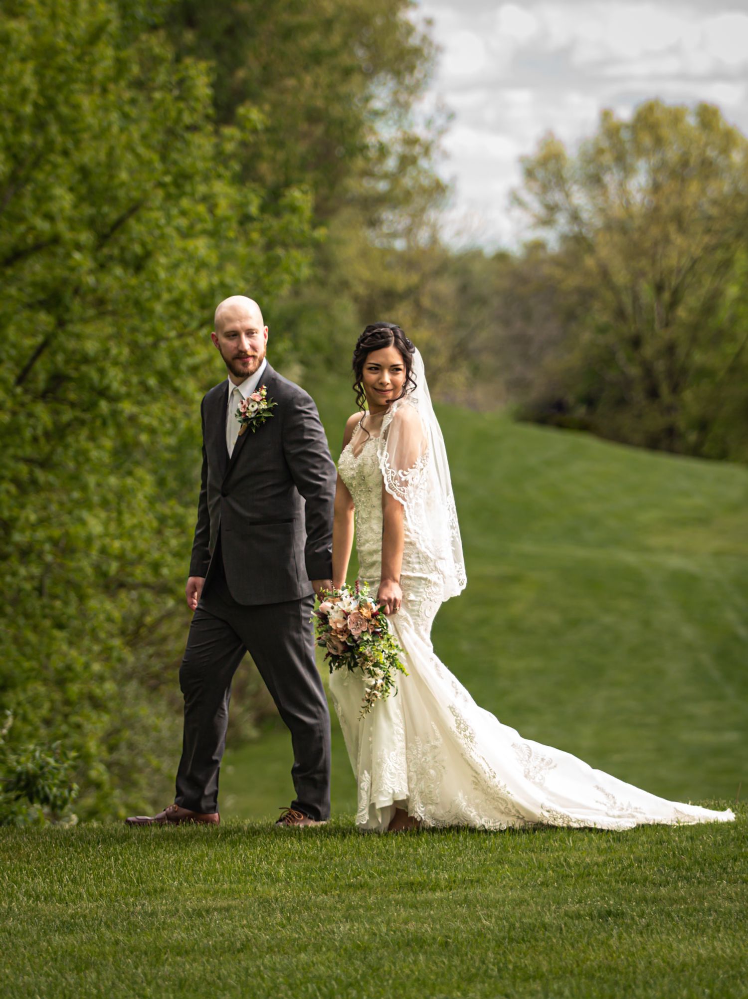 A couple in wedding attire poses on a lush green hillside on their special day.