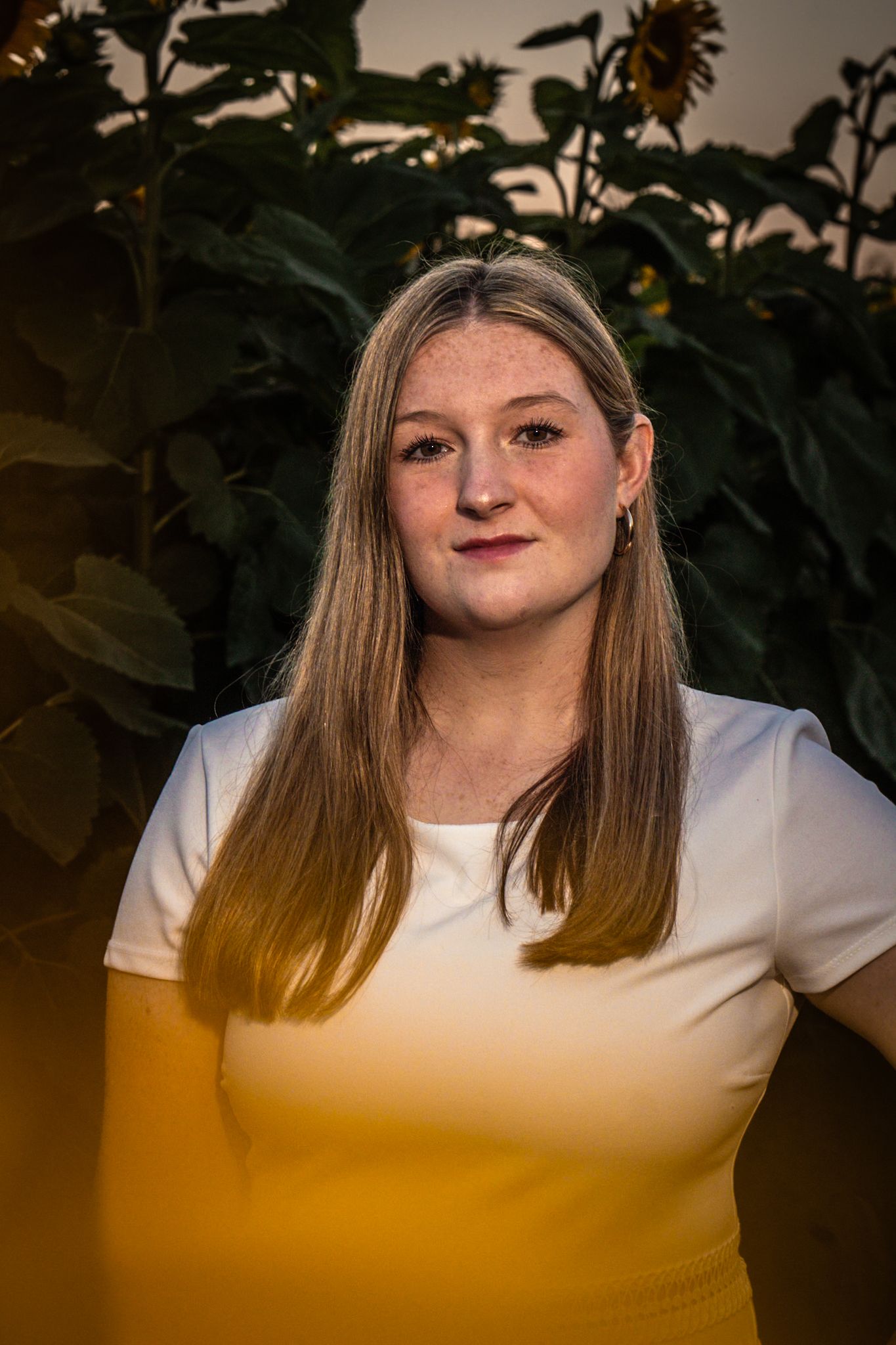 A person in white shirt poses in front of sunflowers at sunset.