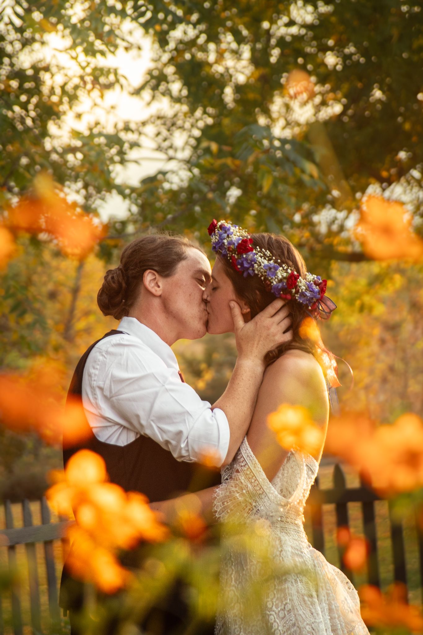 A romantic kiss between a couple at sunset with orange bokeh lights and autumn foliage in the background.
