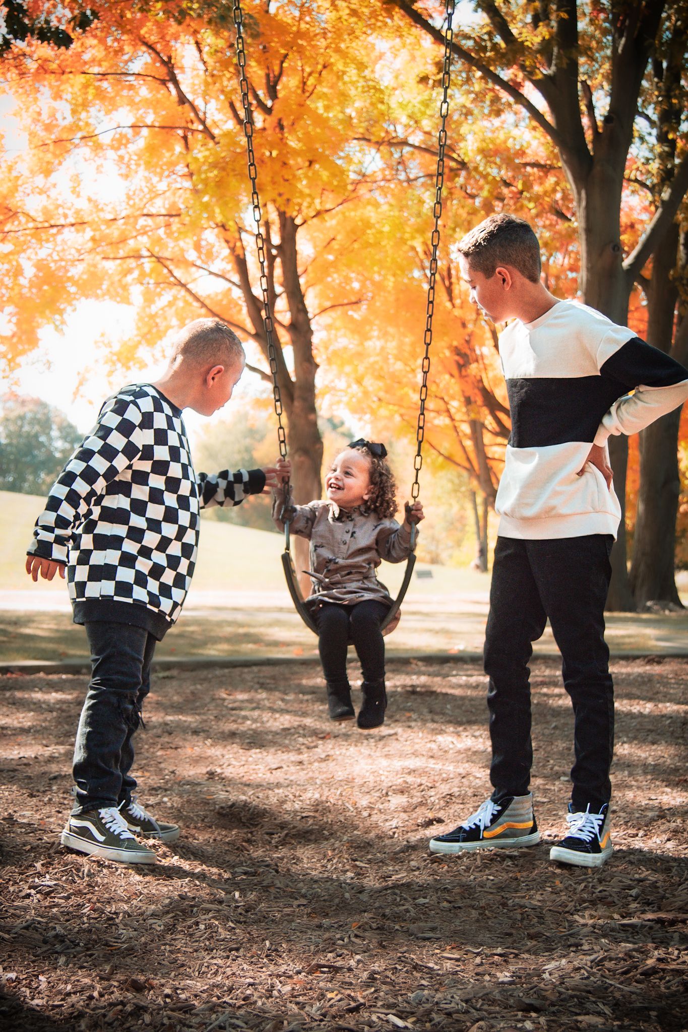 Child on swing enjoying playful moments with others in autumn park with golden leaves.