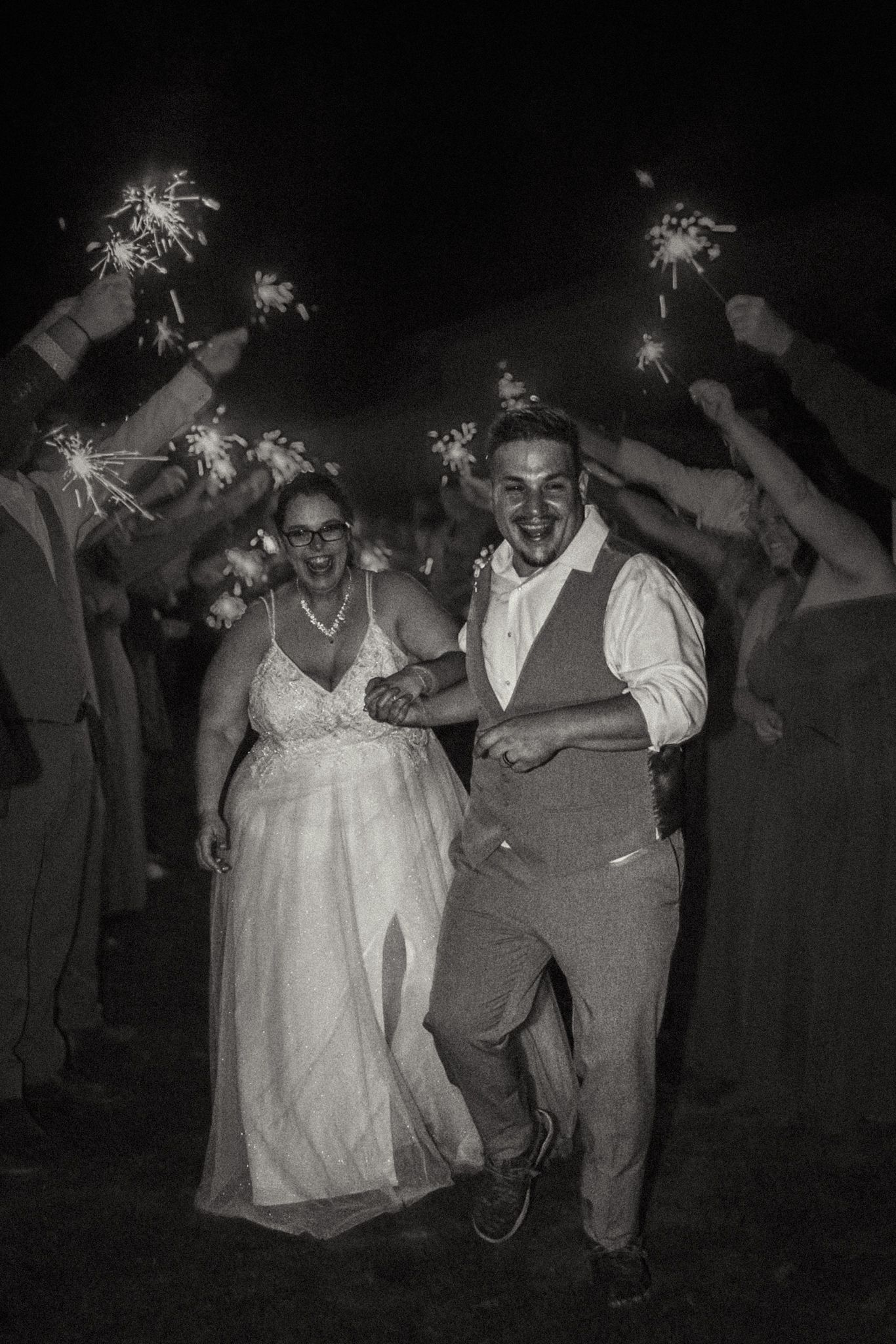 Wedding guests dance joyfully while holding sparklers during an outdoor nighttime celebration.