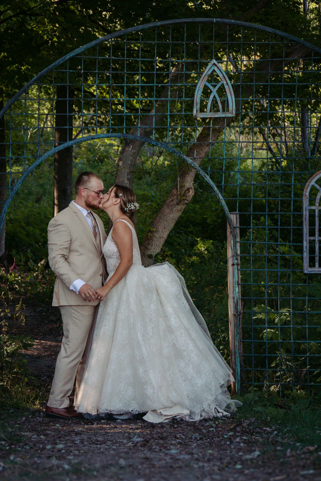 A romantic wedding moment under a turquoise garden arbor surrounded by greenery at The Cathedral Barn in Traverse City, Michigan.