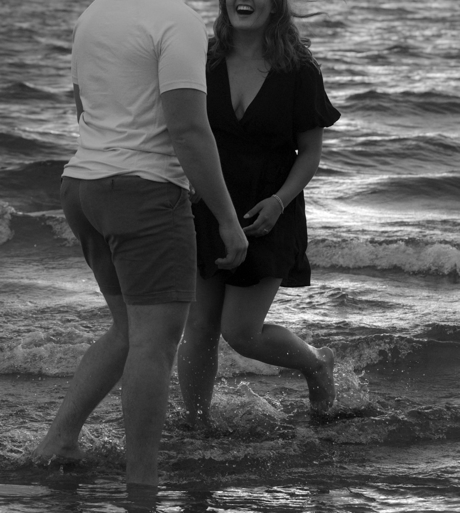 A playful black and white photo of two people splashing in ocean waves.