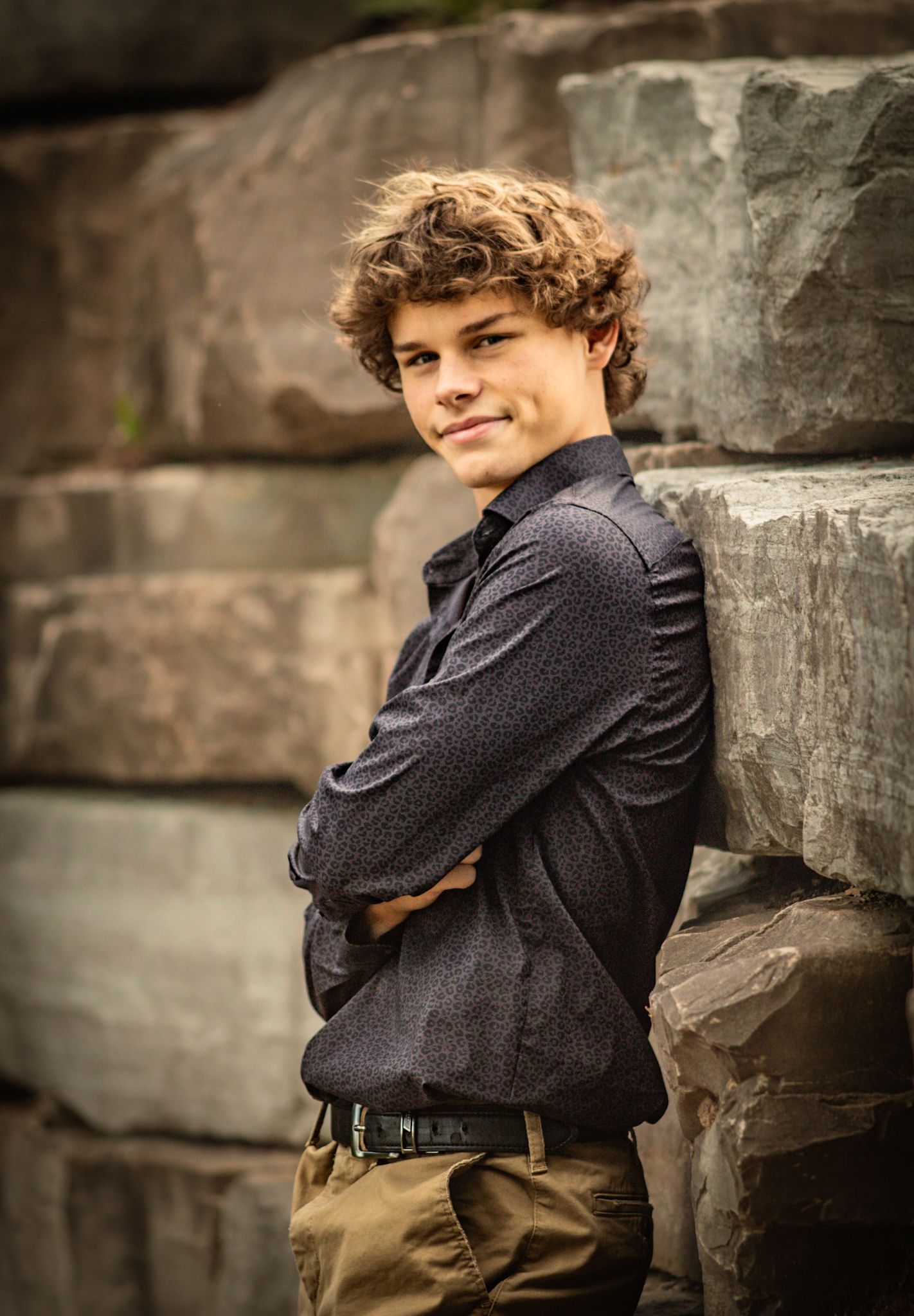 A figure in dark clothing poses against weathered stone walls.