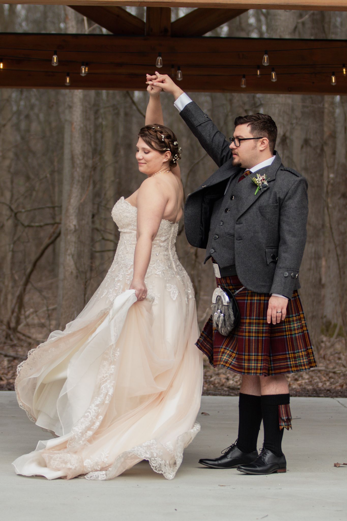 A bride in a flowing gown dances with her groom wearing a traditional Scottish kilt.