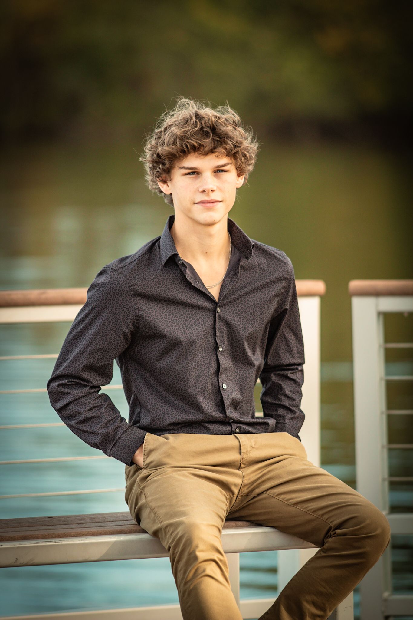 A person in dark shirt and khaki pants sits casually on railing by water.