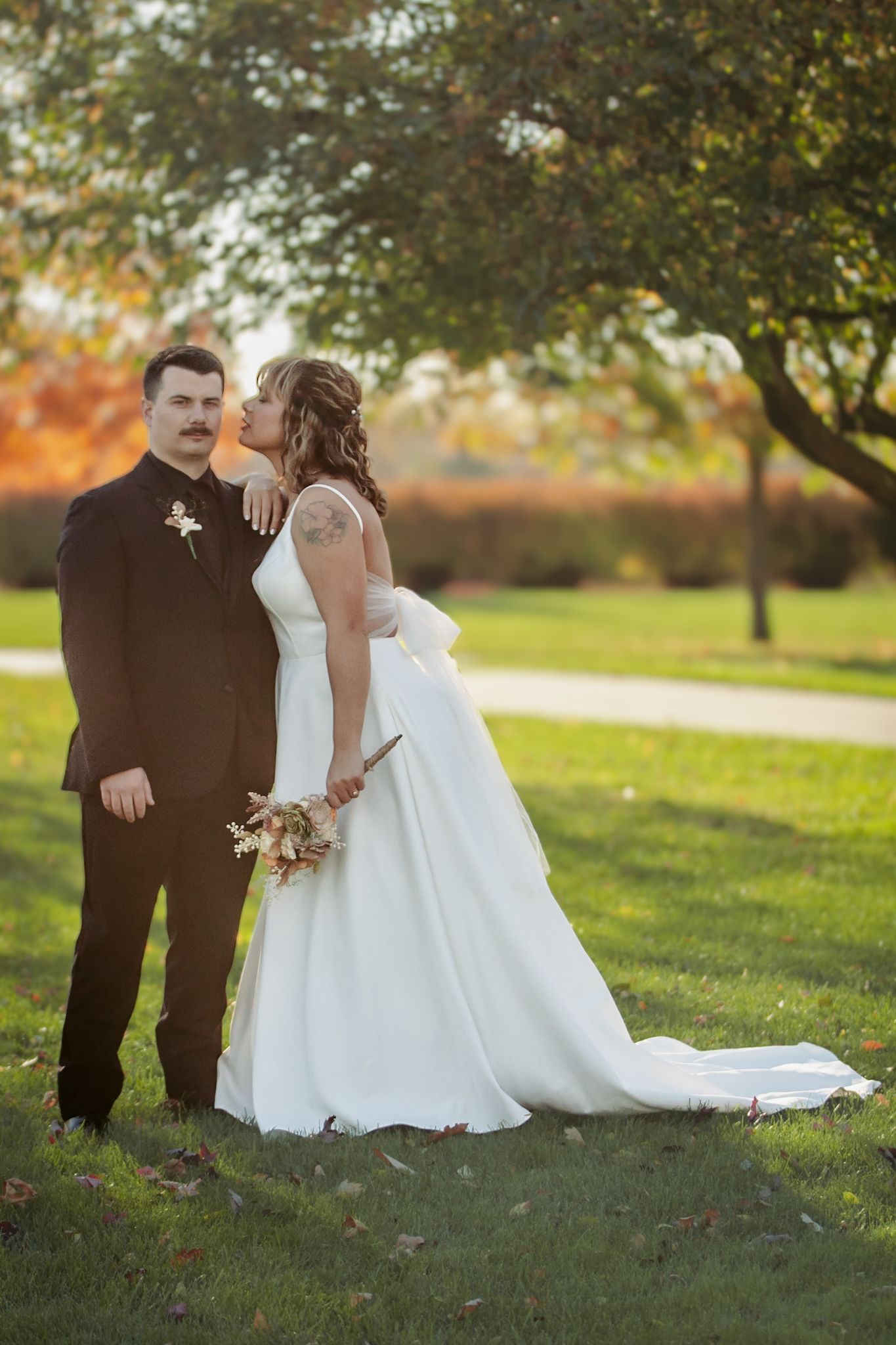 A wedding couple poses together under autumn trees on their special day.