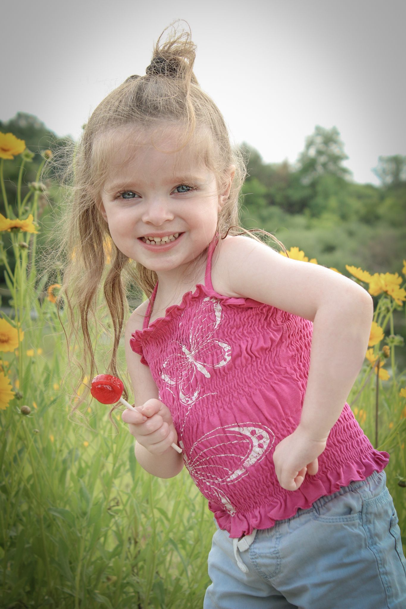 Young one in pink smocked top poses playfully in a wildflower field.