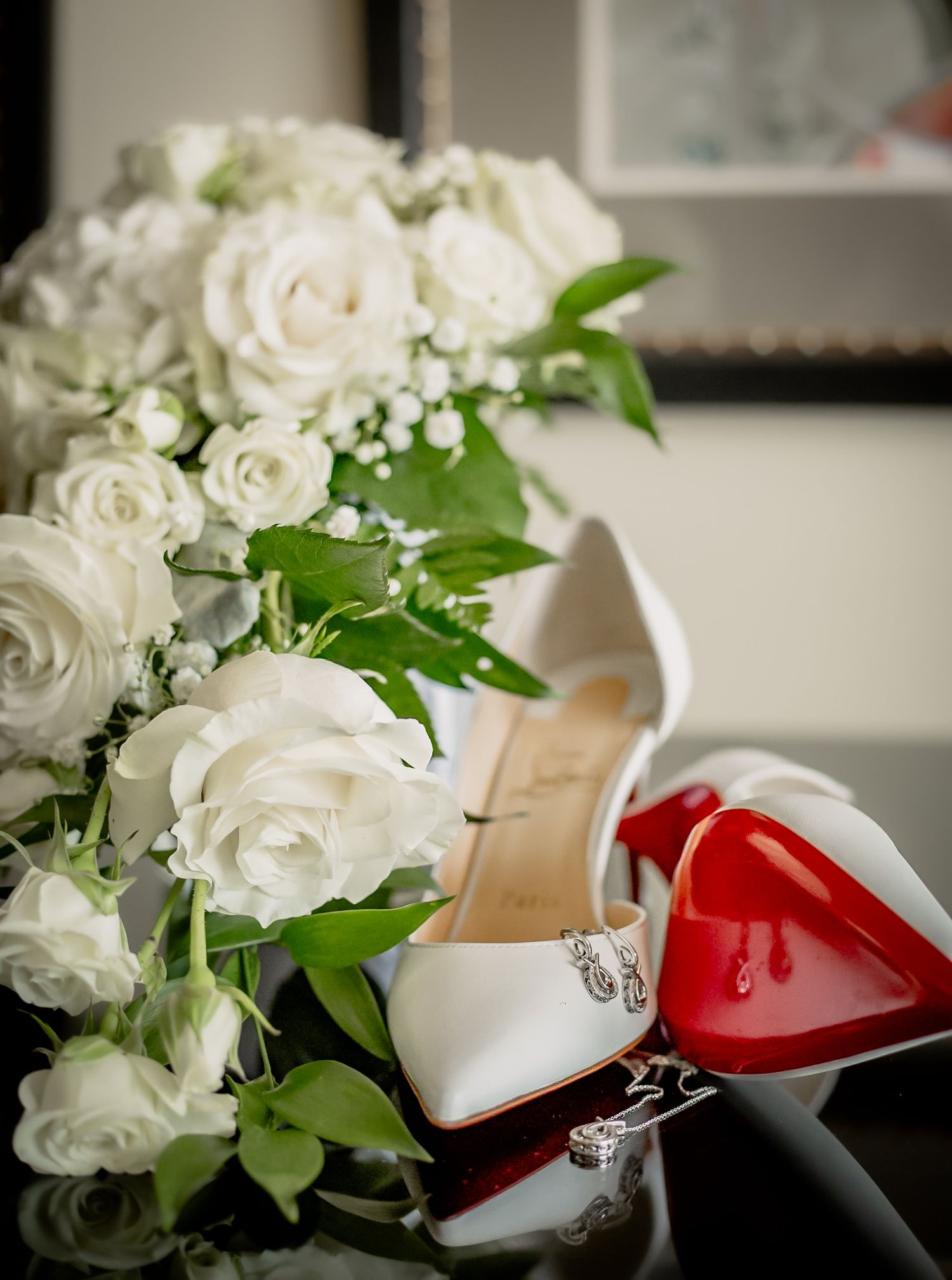 Wedding details featuring white roses and elegant Louboutin shoes in red and white.