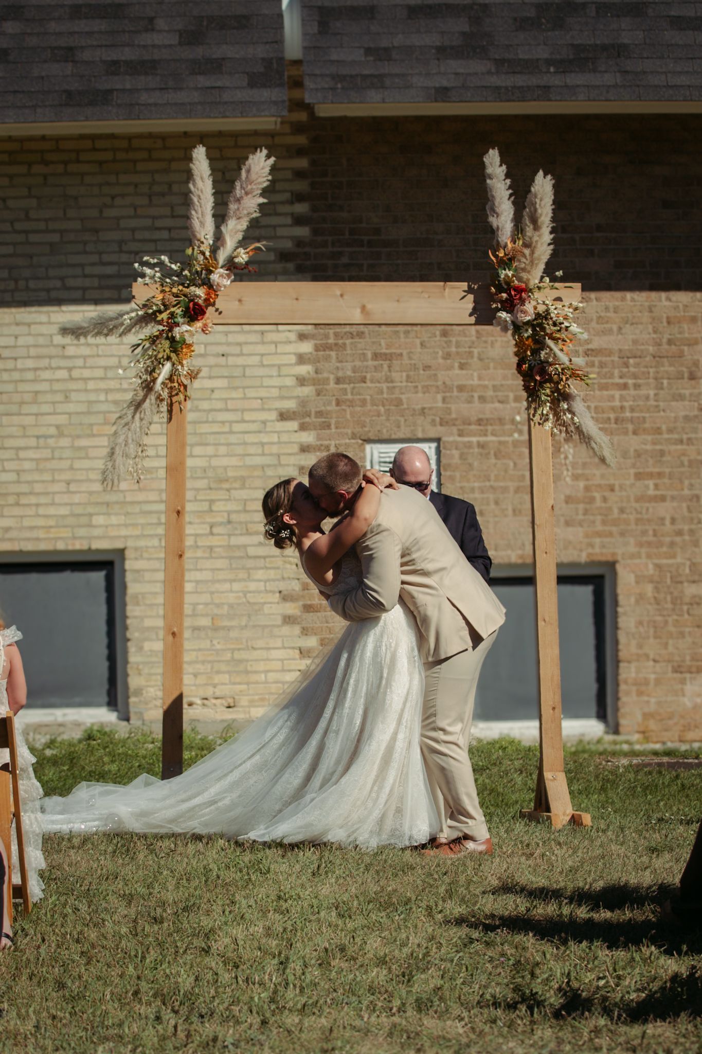 Wedding ceremony under pampas grass arch decorations against brick wall backdrop at The Cathedral Barn in Traverse City, Michigan.