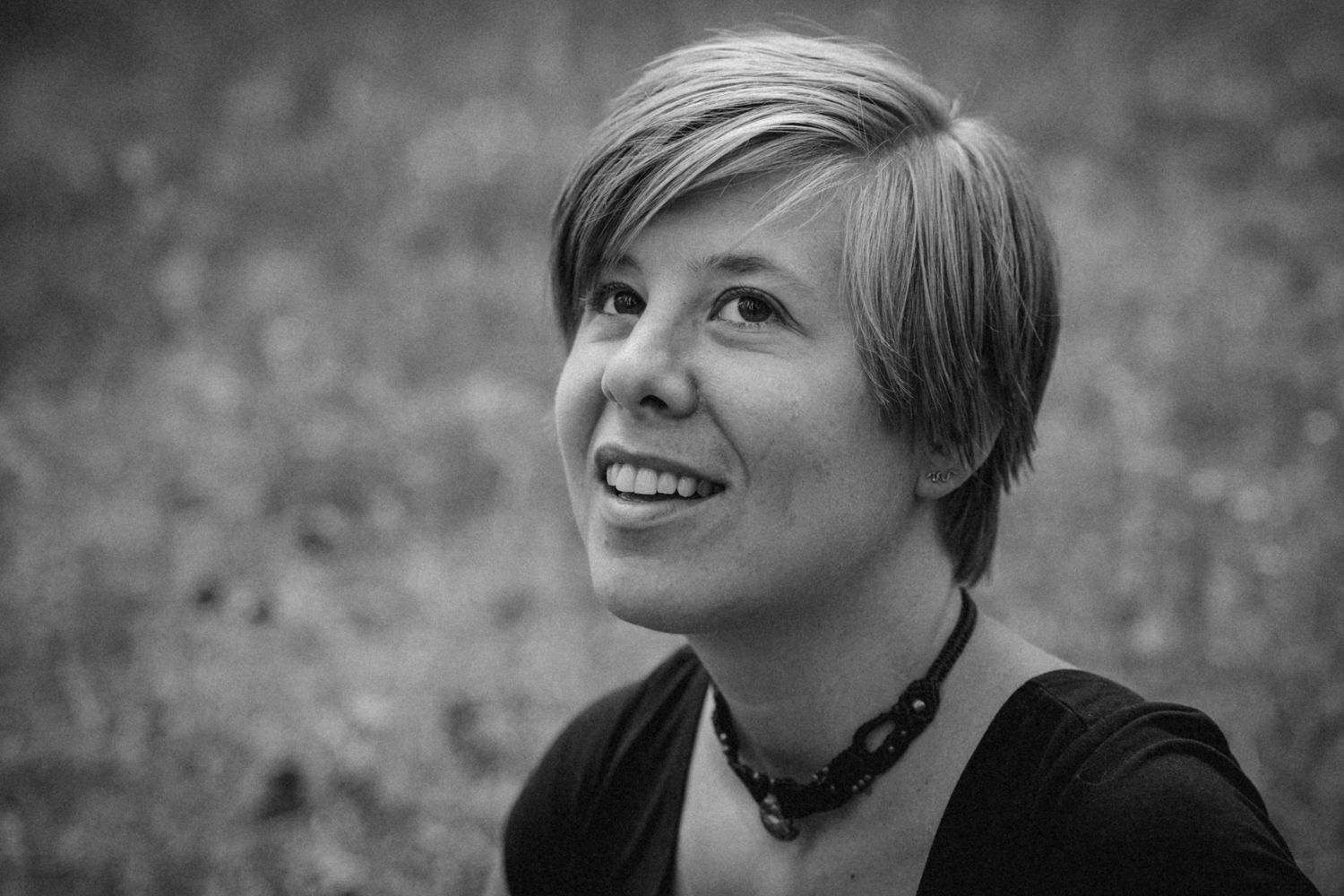 A black and white portrait showing a warm smile and short hair against a blurred background.