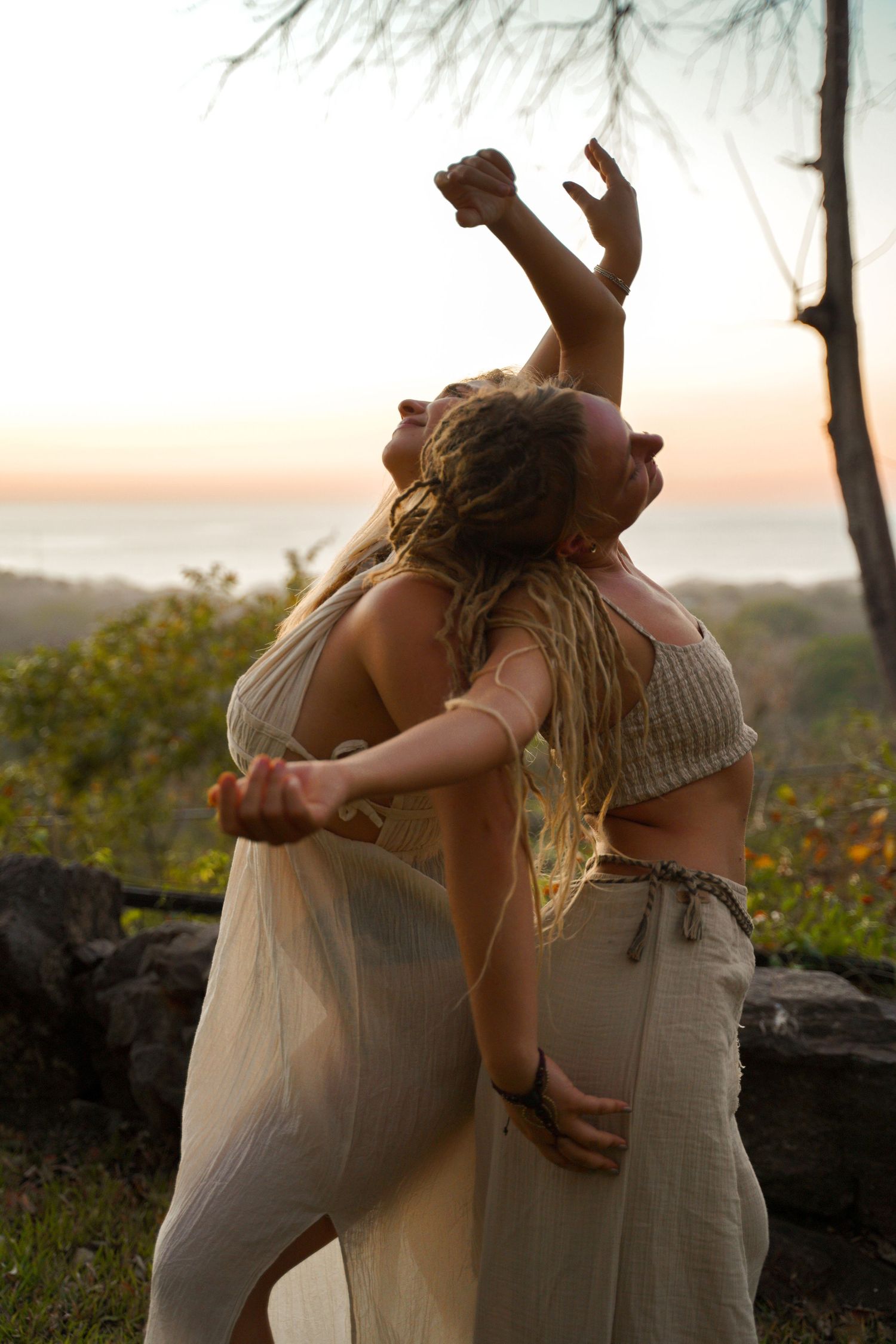 Two figures embrace and dance at sunset on a hilltop with trees in the background.